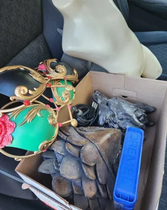 A box containing gloves, a blue item, and miscellaneous objects, with a white object and a decorative mask nearby.