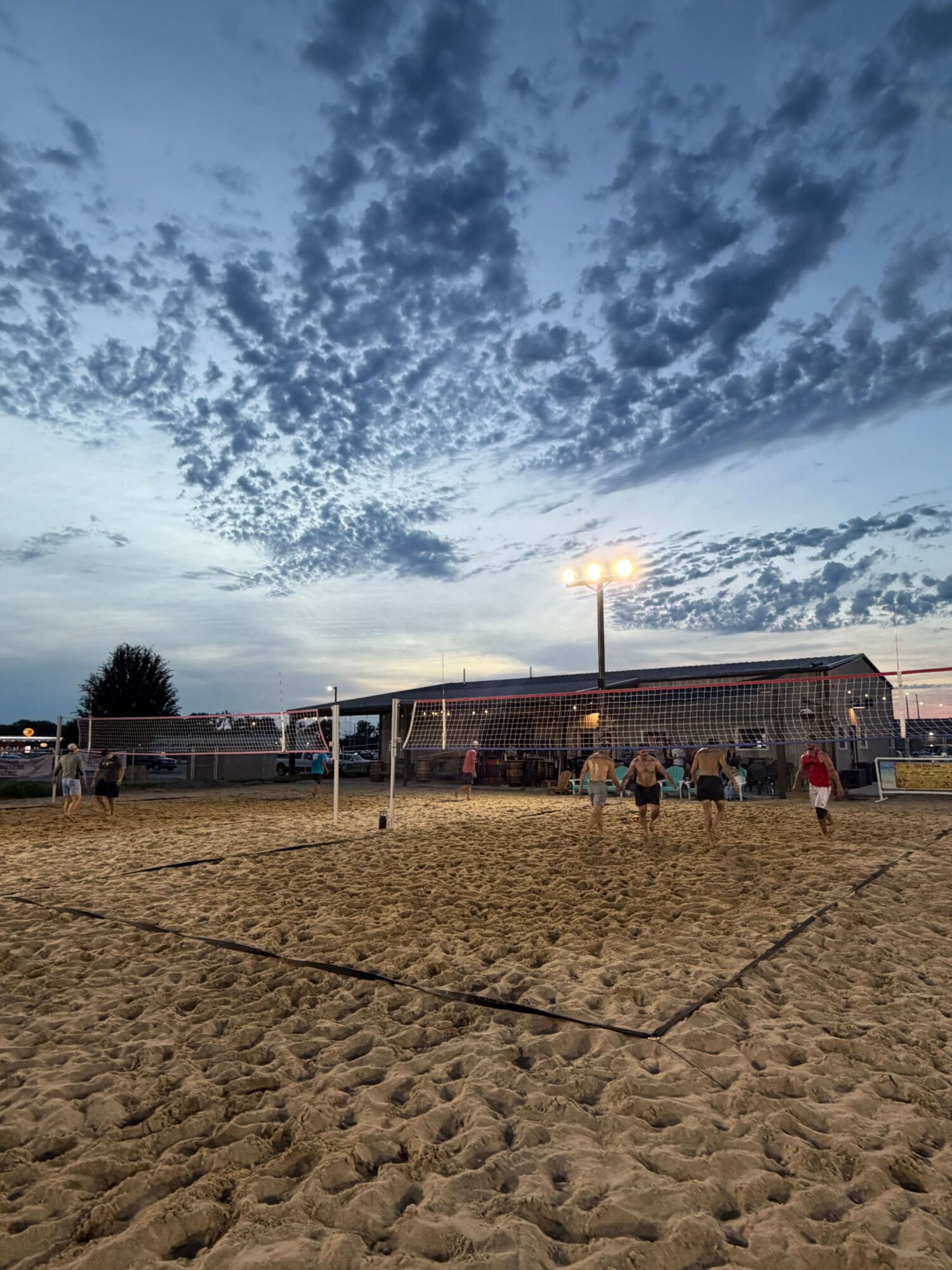 Beach scene with sand, a building, and a cloudy sky with the sun visible, viewed sideways.