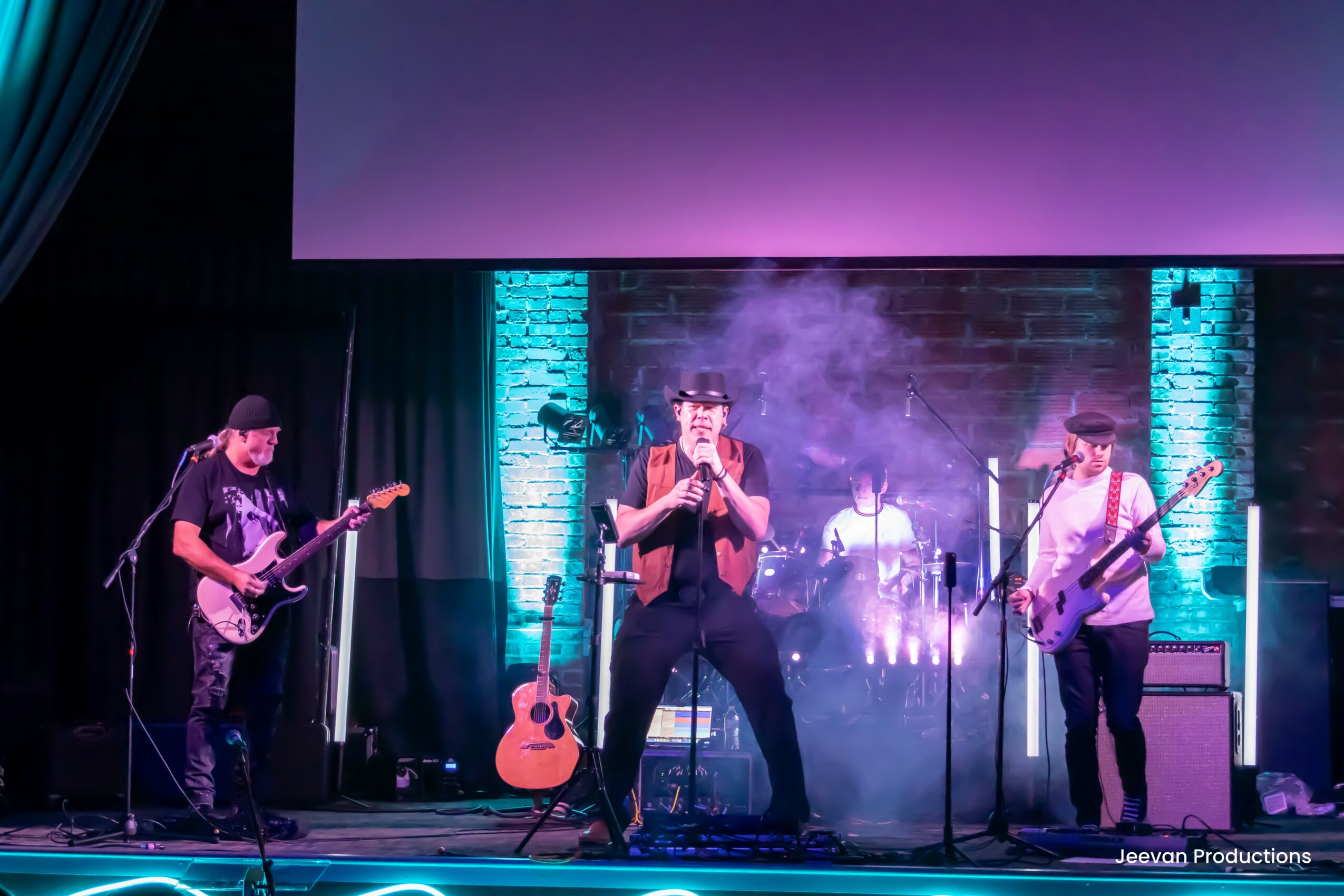 Band performs on stage with colorful lighting, smoke effects, and musical instruments including guitars and drums.