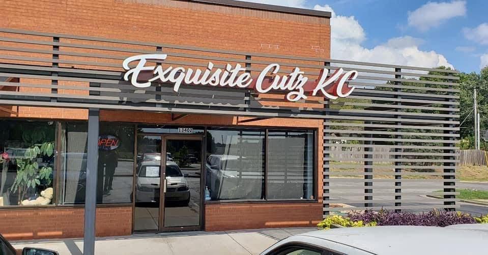 Storefront with sign reading 'Exquisite Cutz KC' and large glass windows, brick exterior, and horizontal metal slats.