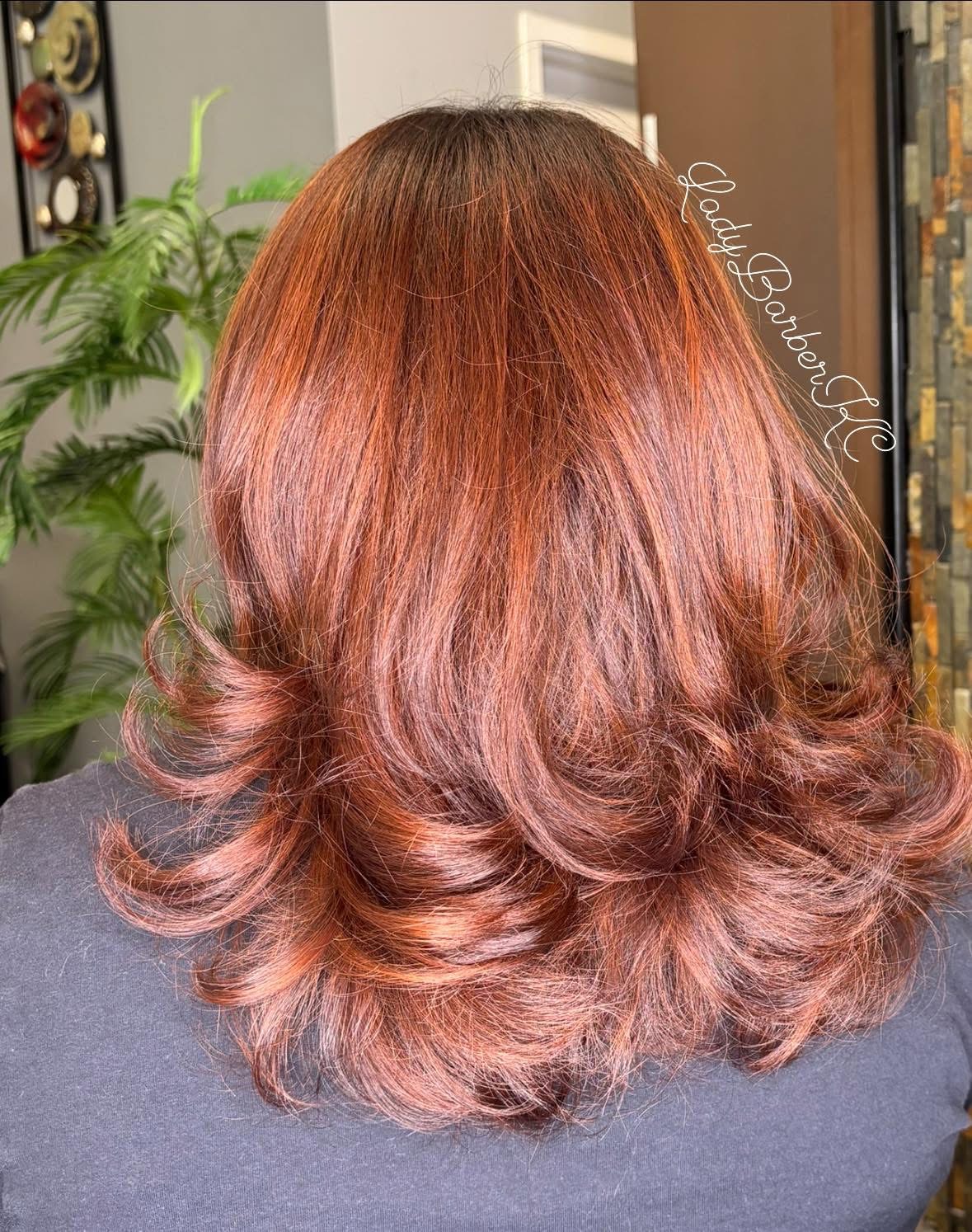 Back view of a person's shoulder-length, wavy hair with reddish-brown color and soft curls at the ends.