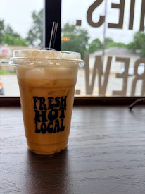 Iced coffee in a clear cup with a lid and straw, placed on a wooden table near a window.