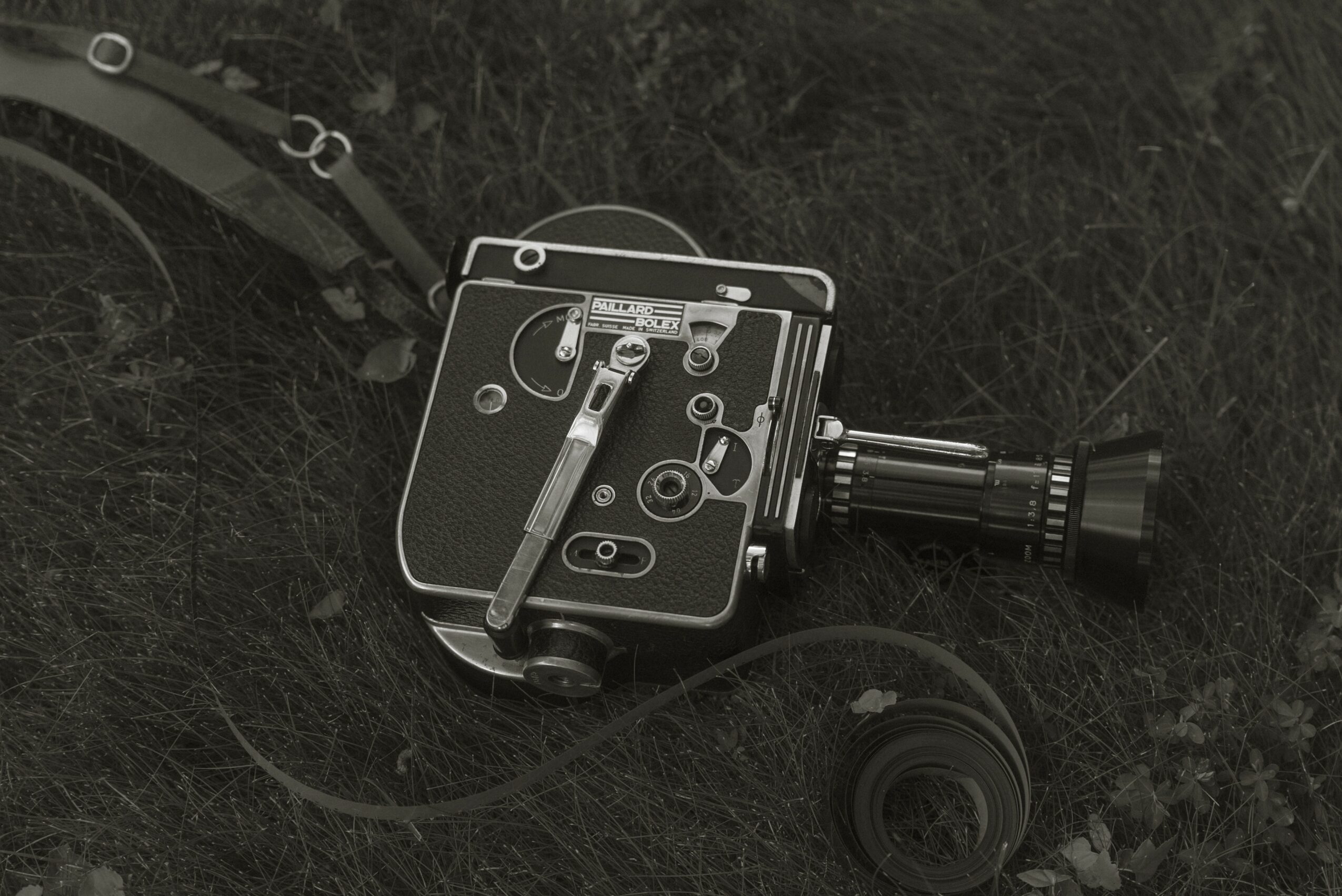 Camera equipment with a lens, placed on grass, viewed from above, with various controls visible.