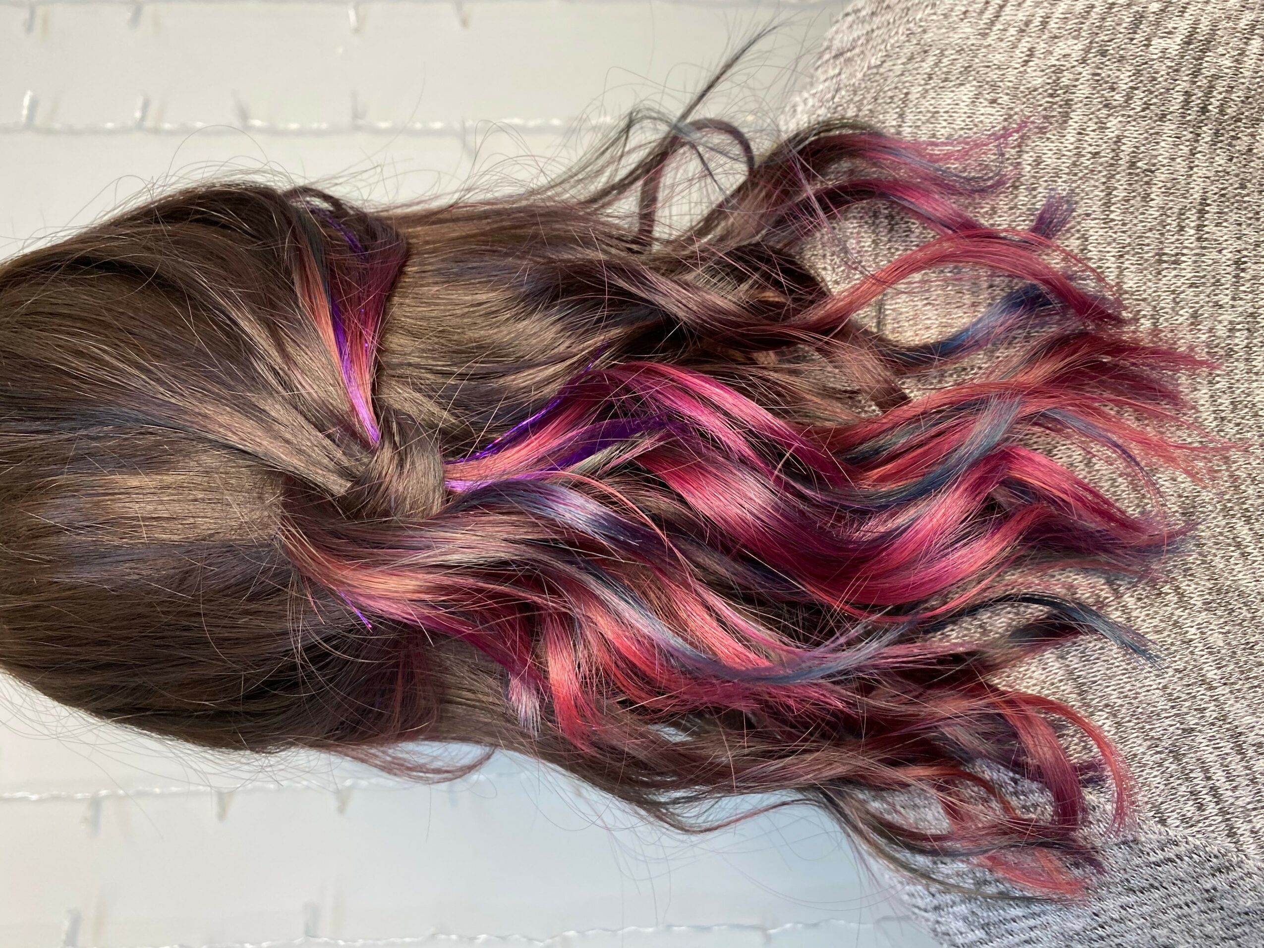 Side view of a person's long, wavy hair with pink highlights, resting on a textured surface.
