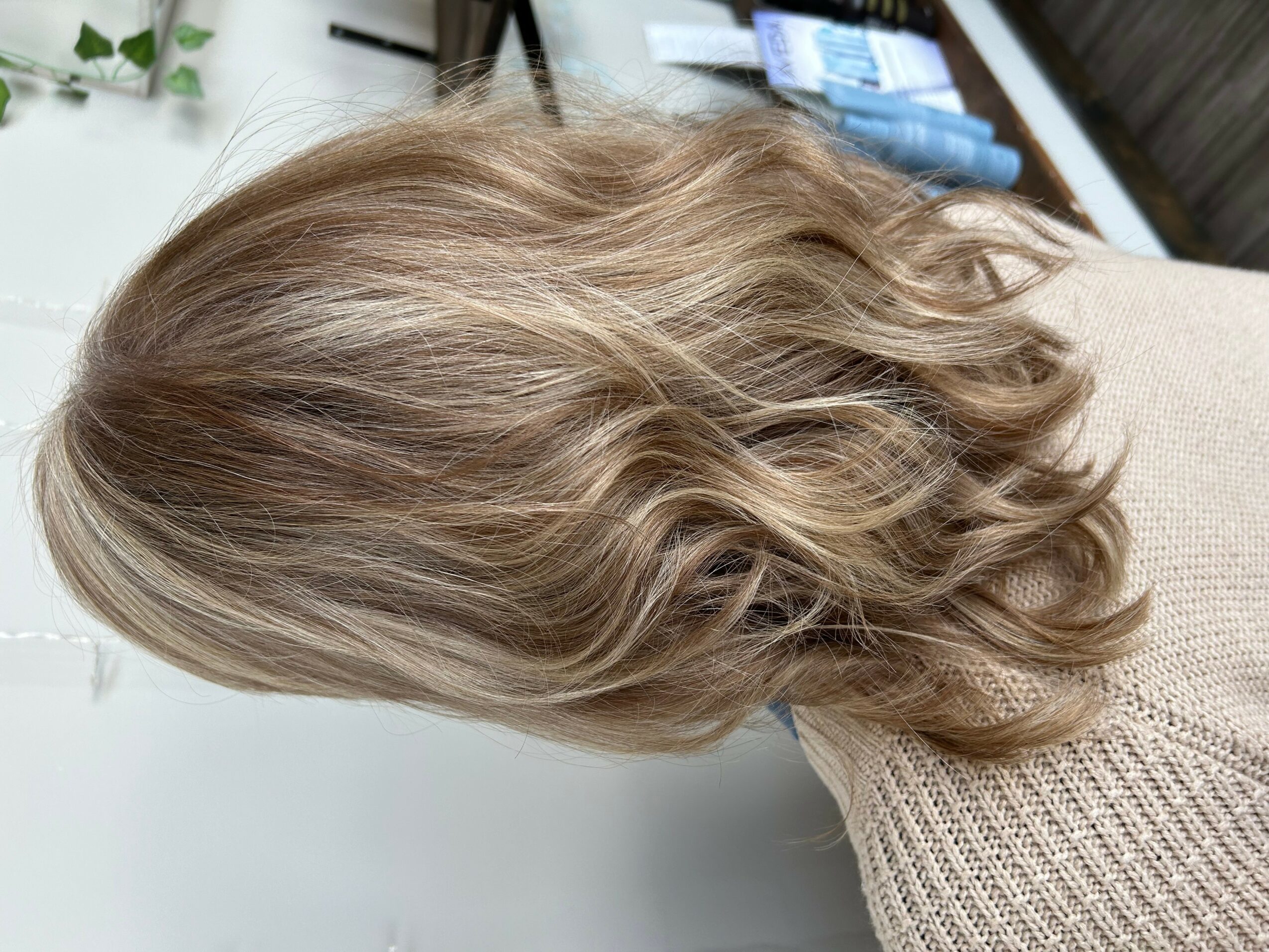Side view of a person with shoulder-length, wavy blonde hair, wearing a beige sweater, indoors.