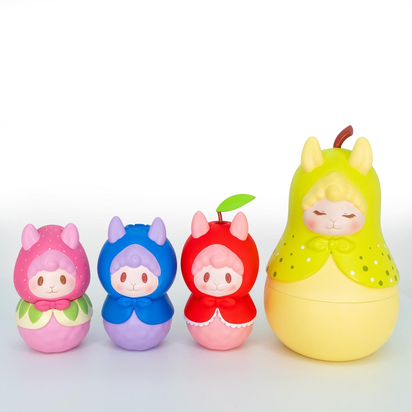 Four colorful, rounded figurines resembling children in animal costumes, with the largest on the right, all smiling, against a white background.