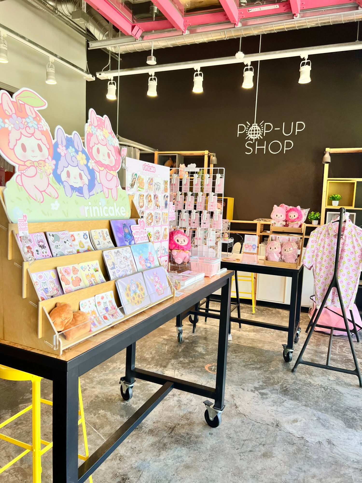 Display of colorful stationery and gifts at a pop-up shop with black wall and pink ceiling beams.