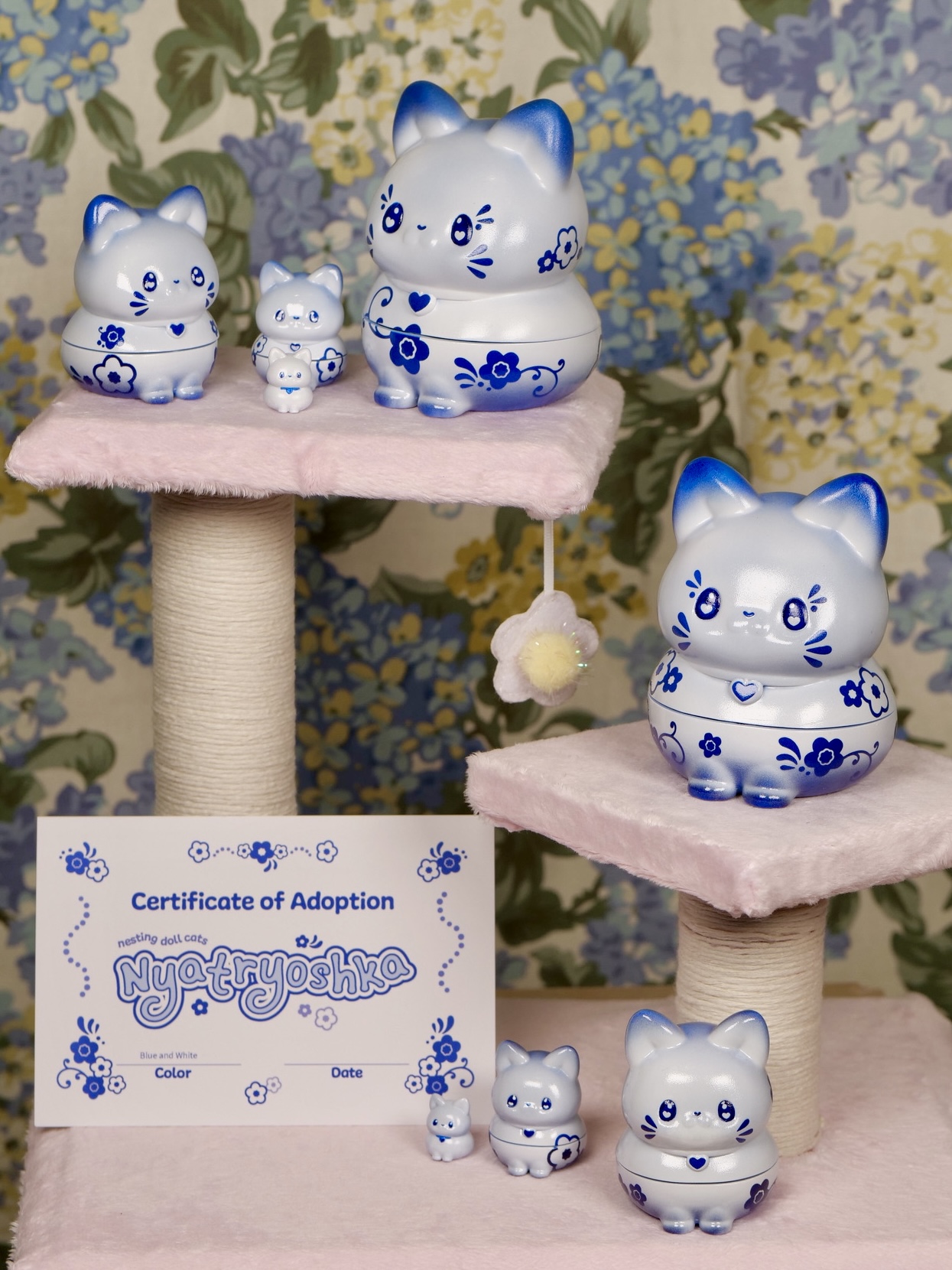 Six blue and white ceramic cat figurines on pink platforms with a floral wallpaper background, and a certificate of adoption.