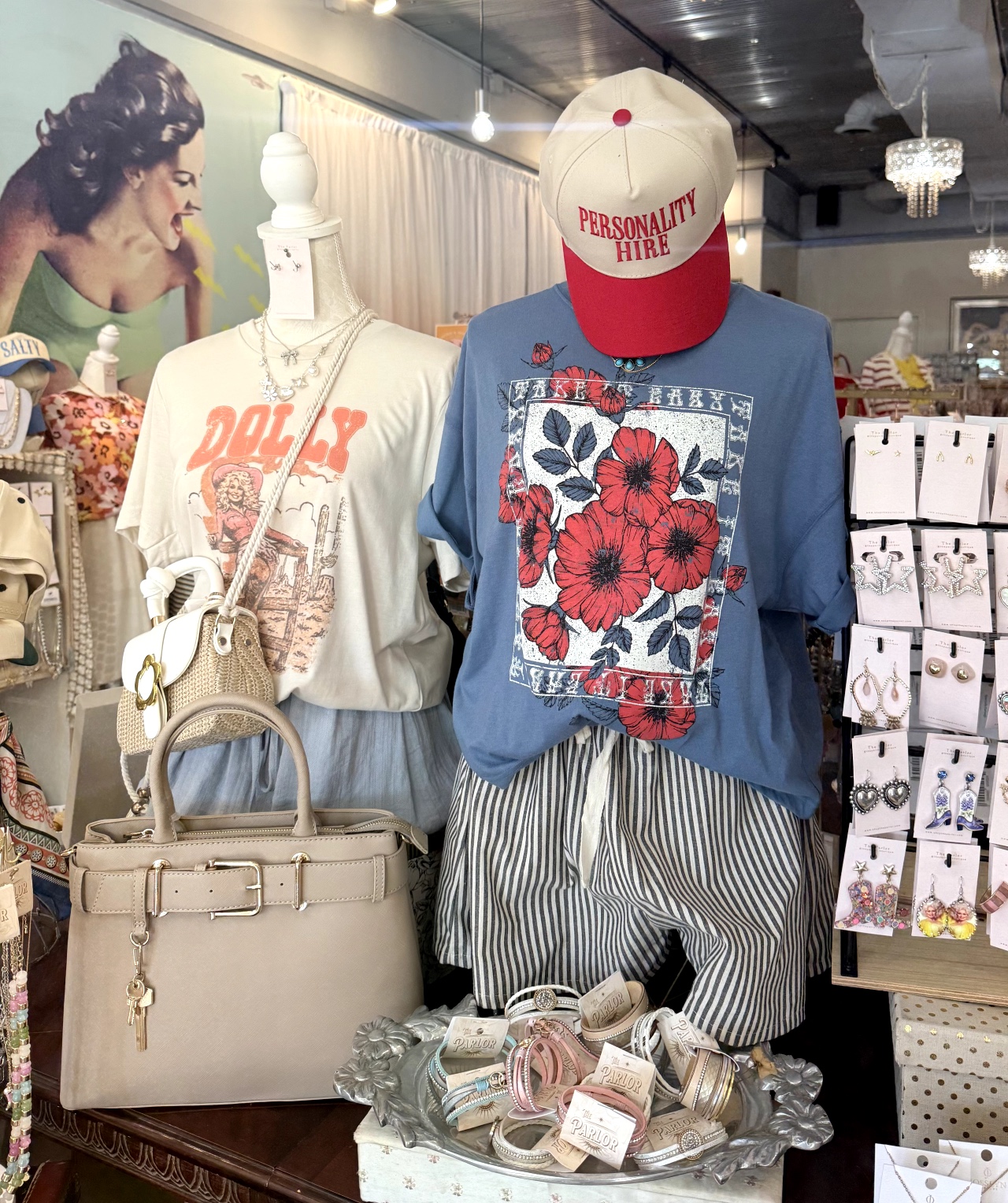 Display of mannequins wearing casual clothing, accessories, and a hat in a store. Mannequins have floral and striped patterns. Background shows store interior.