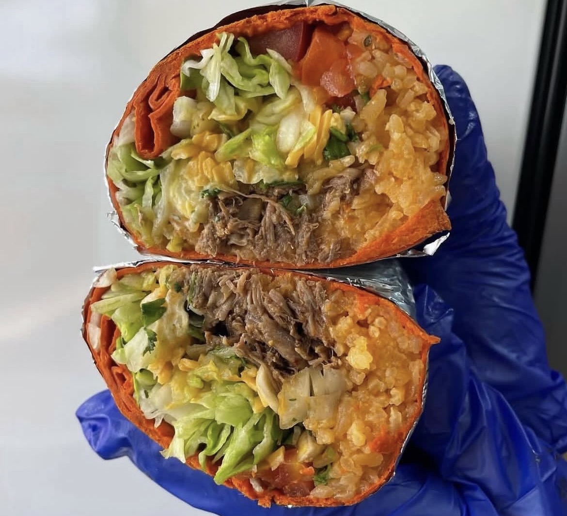 Halved burrito with lettuce, beef, rice, and vegetables, held by a hand in a blue glove.