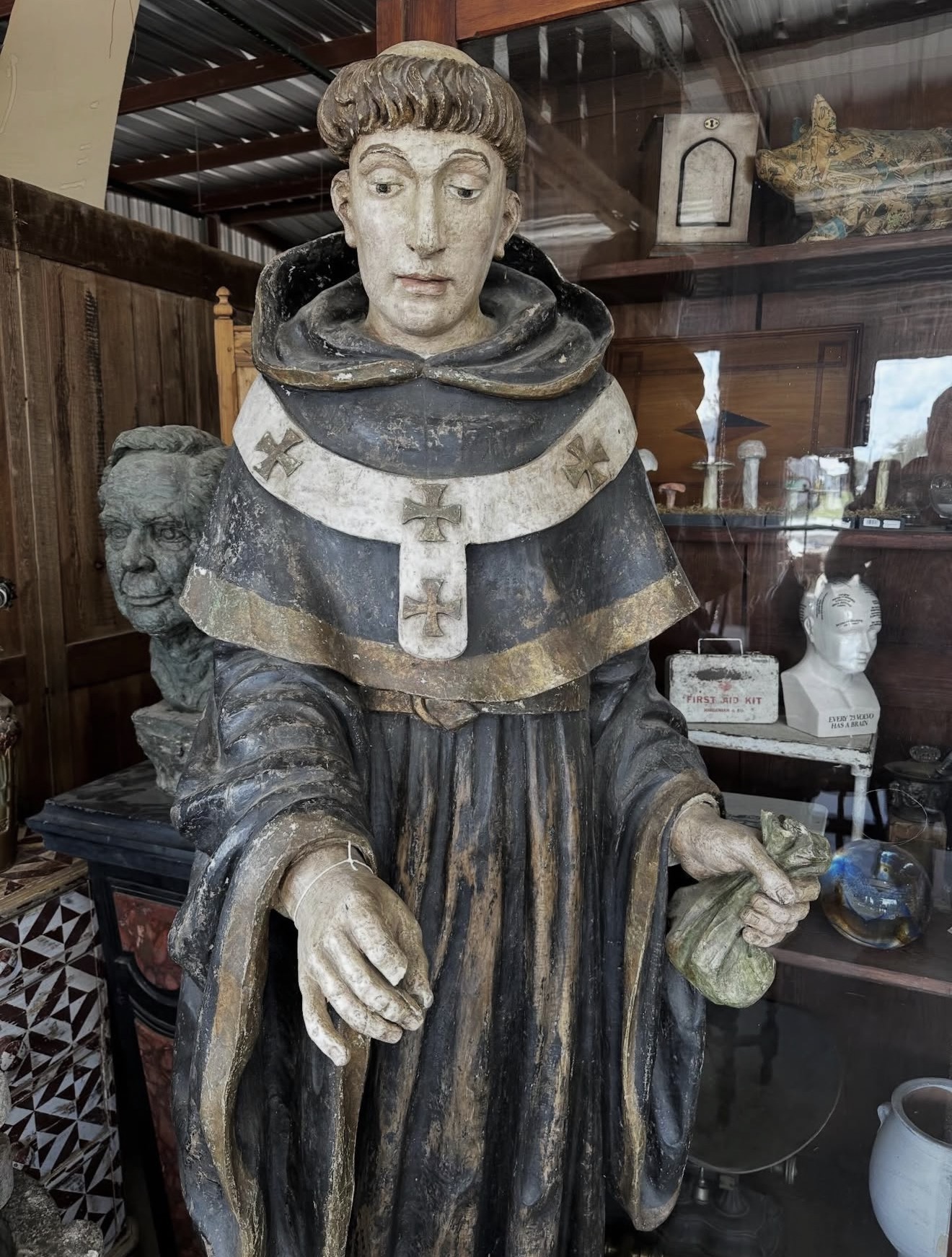 Statue of a person in religious attire holding a small object, with a head sculpture beside them, displayed in a wooden room.