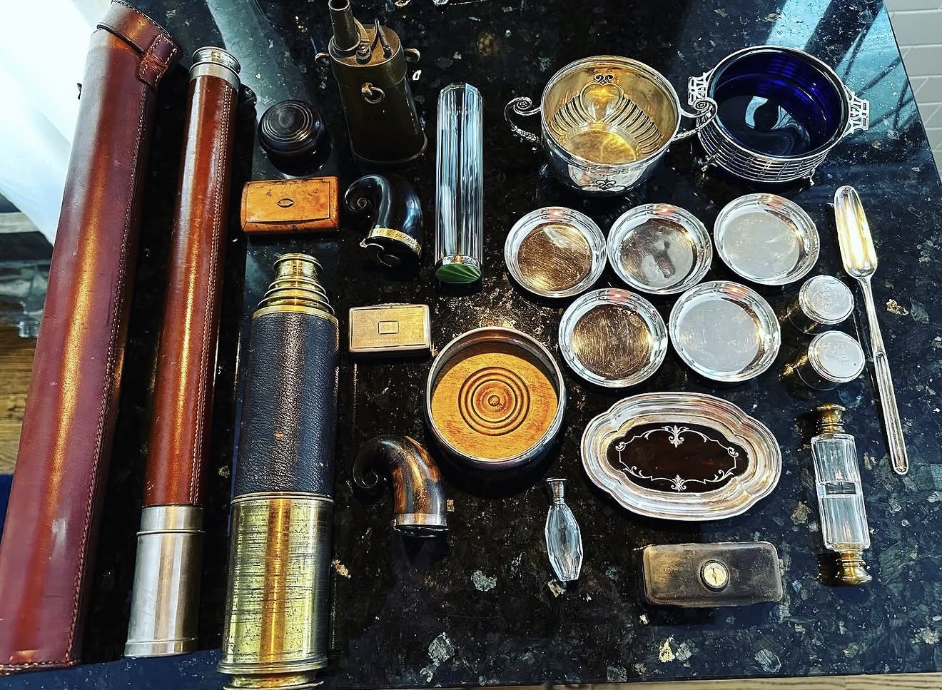 Collection of vintage telescopes, lenses, and small containers on a dark surface, with various metallic and glass objects.