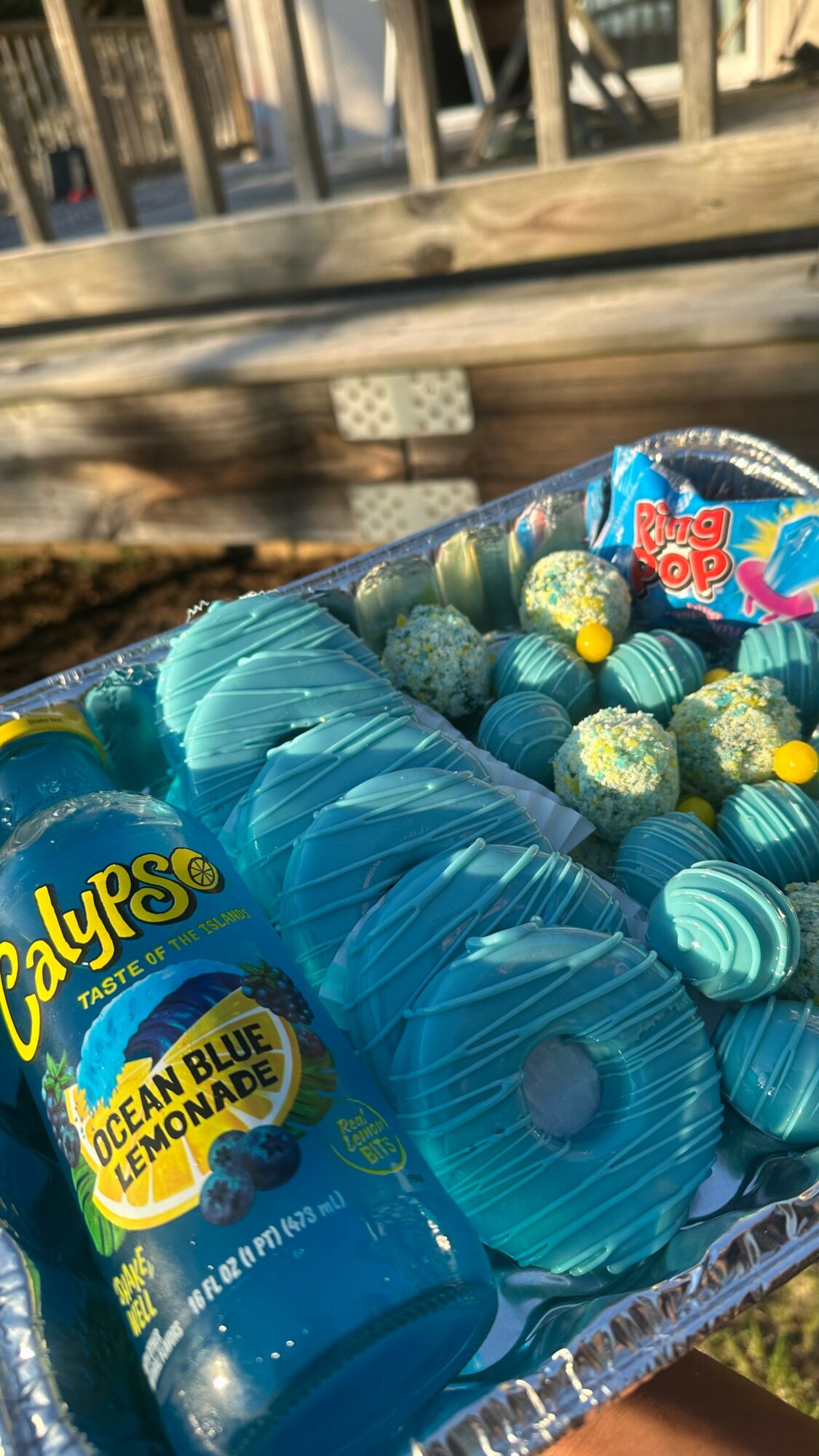 Blue Calypso Ocean Blue Lemonade drink bottle surrounded by blue and green candies outdoors.