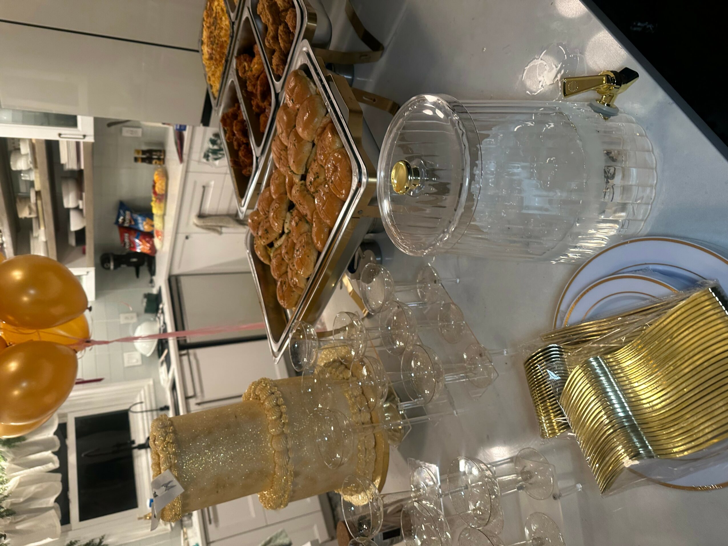 Party table with snacks, drinks, and gold-colored cups, with balloons in the background.