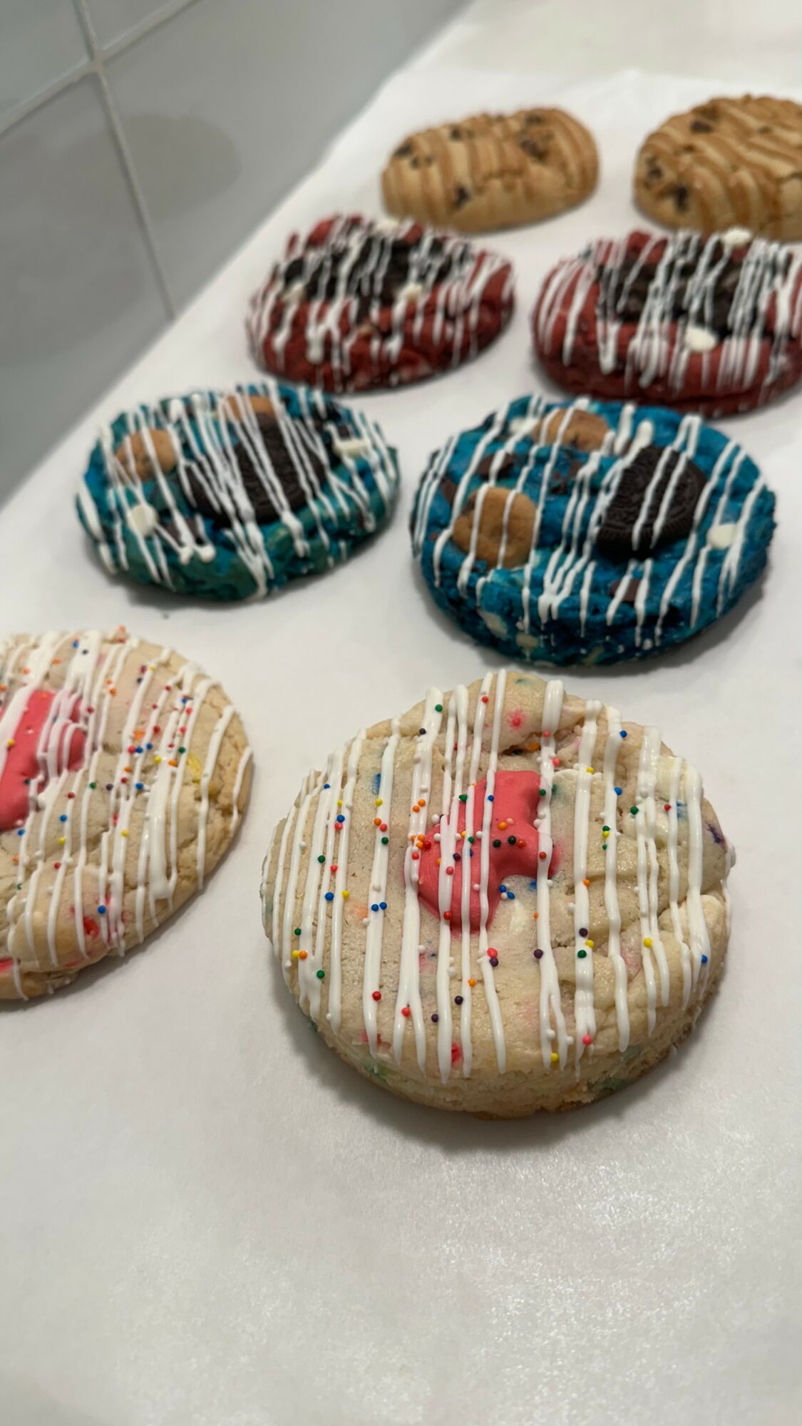 Six decorated cookies with colorful icing and sprinkles on a white surface.