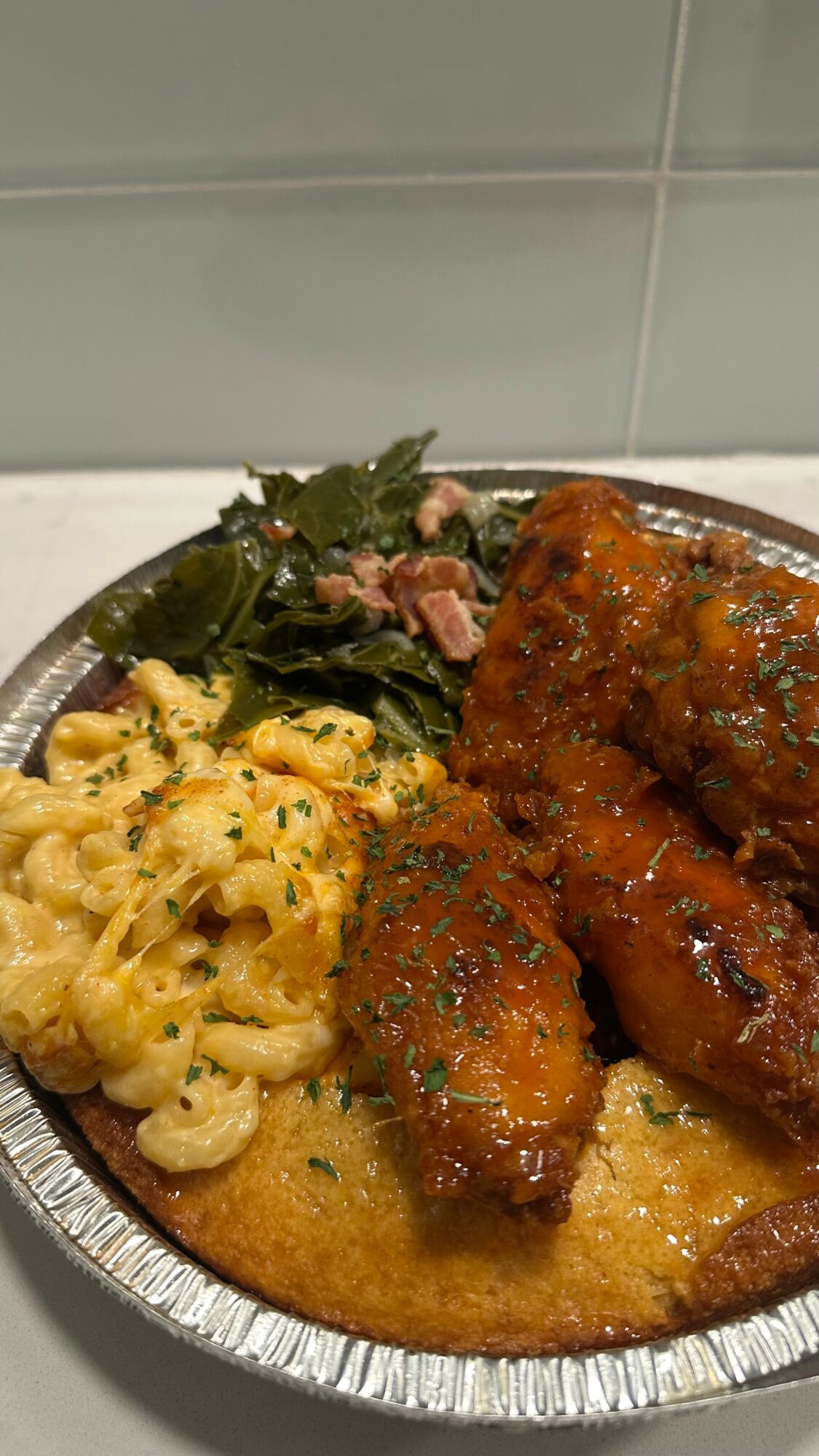Plate with macaroni and cheese, glazed meat, and greens, on a white tiled surface.