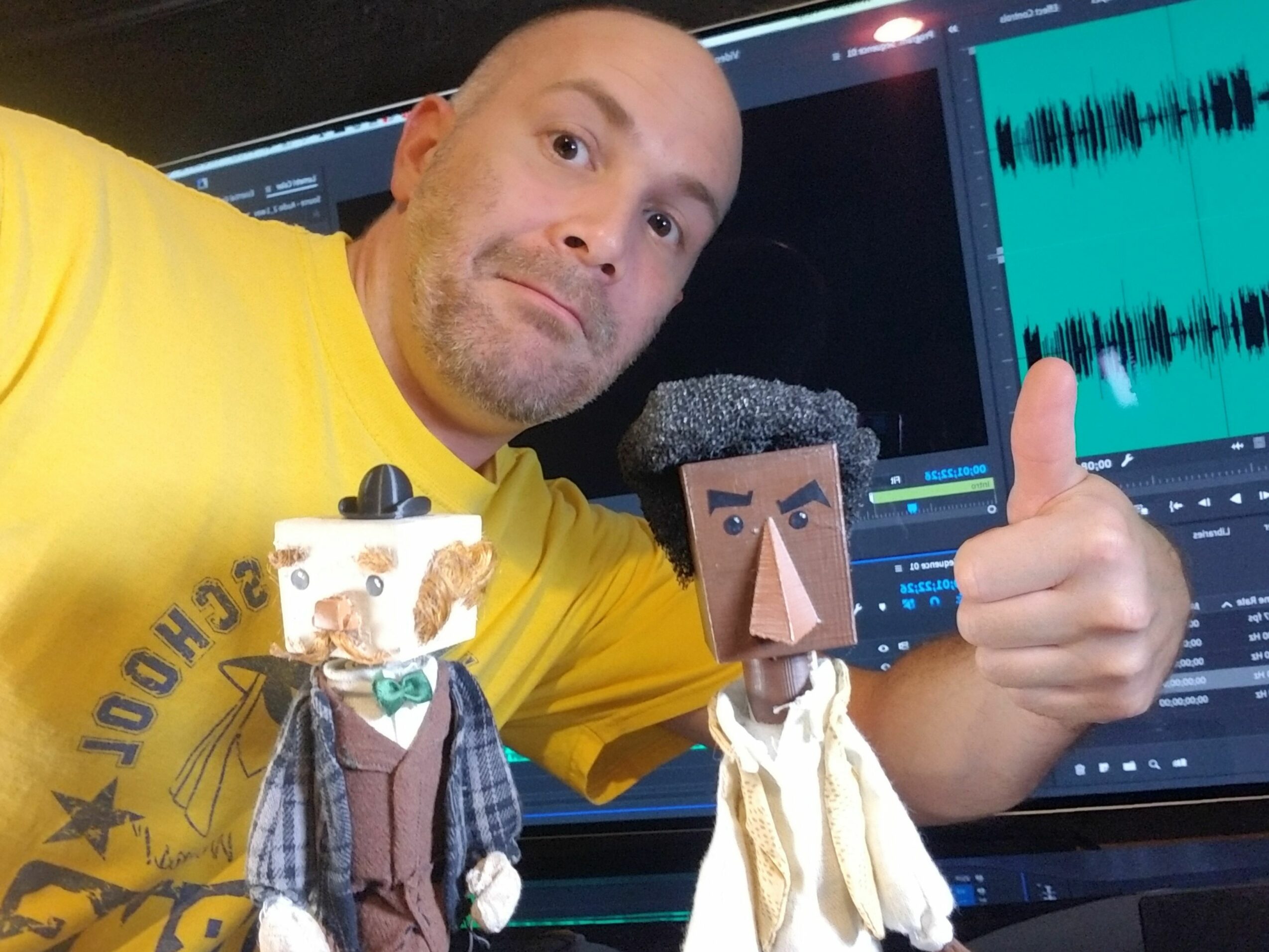 Person holding a small puppet with a computer screen in the background, wearing a yellow shirt, upside down.