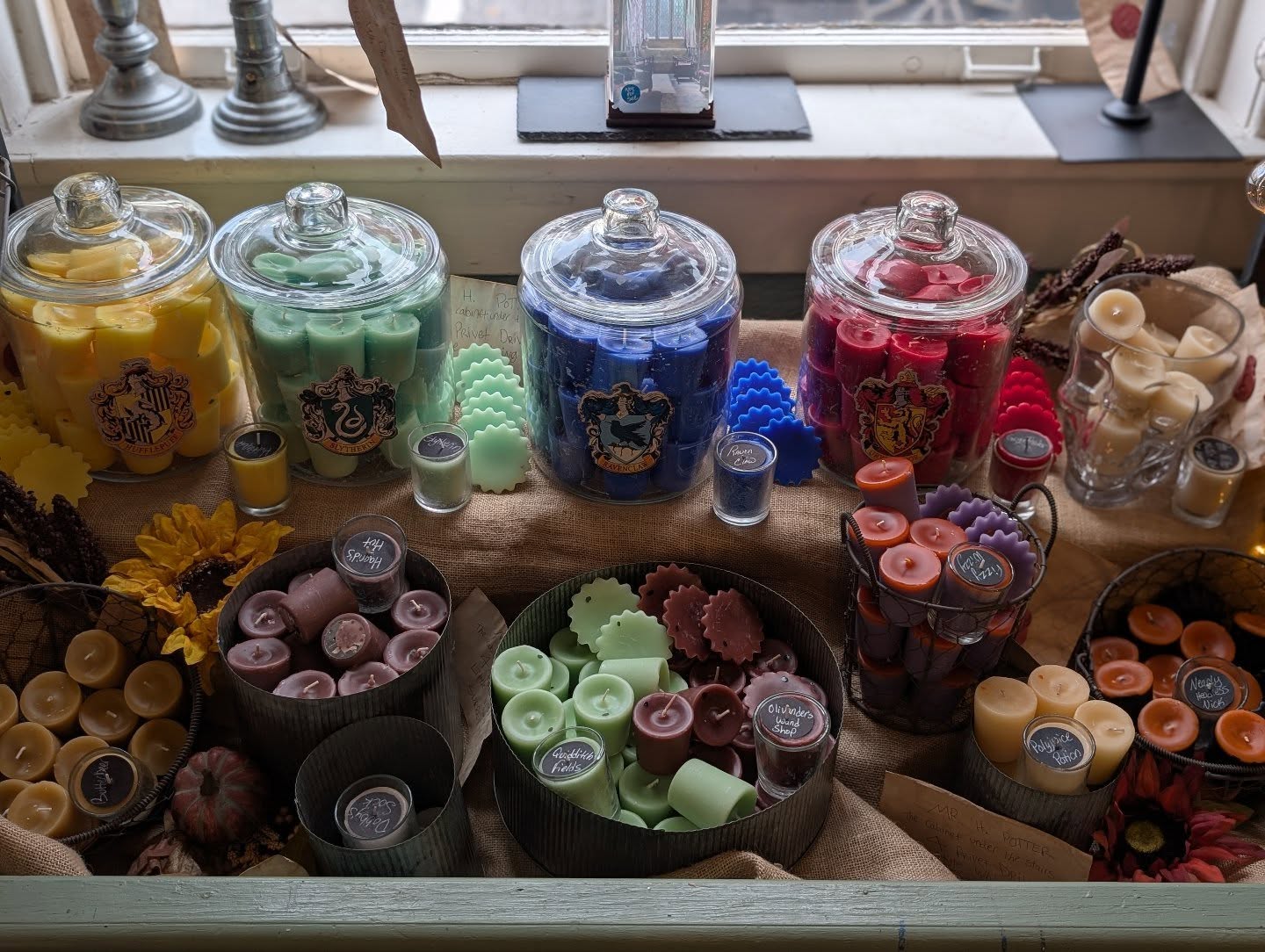 Display of colorful candies in glass jars and bowls on a wooden surface, with a window in the background.