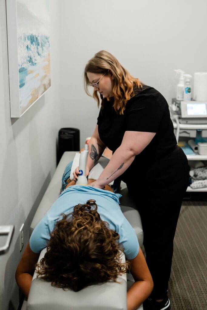 Healthcare professional performing a procedure on a patient lying on a bed in a clinical setting.