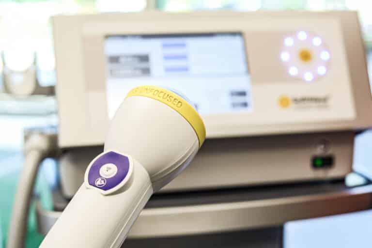 Medical device with a yellow lid and purple button, in front of a screen displaying data, on a table.