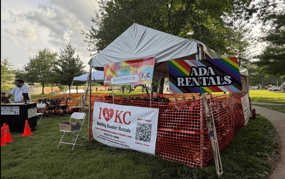 Tent with signs for ADA Rentals and KC Midwest Southern Rentals at outdoor event, surrounded by trees and grass.