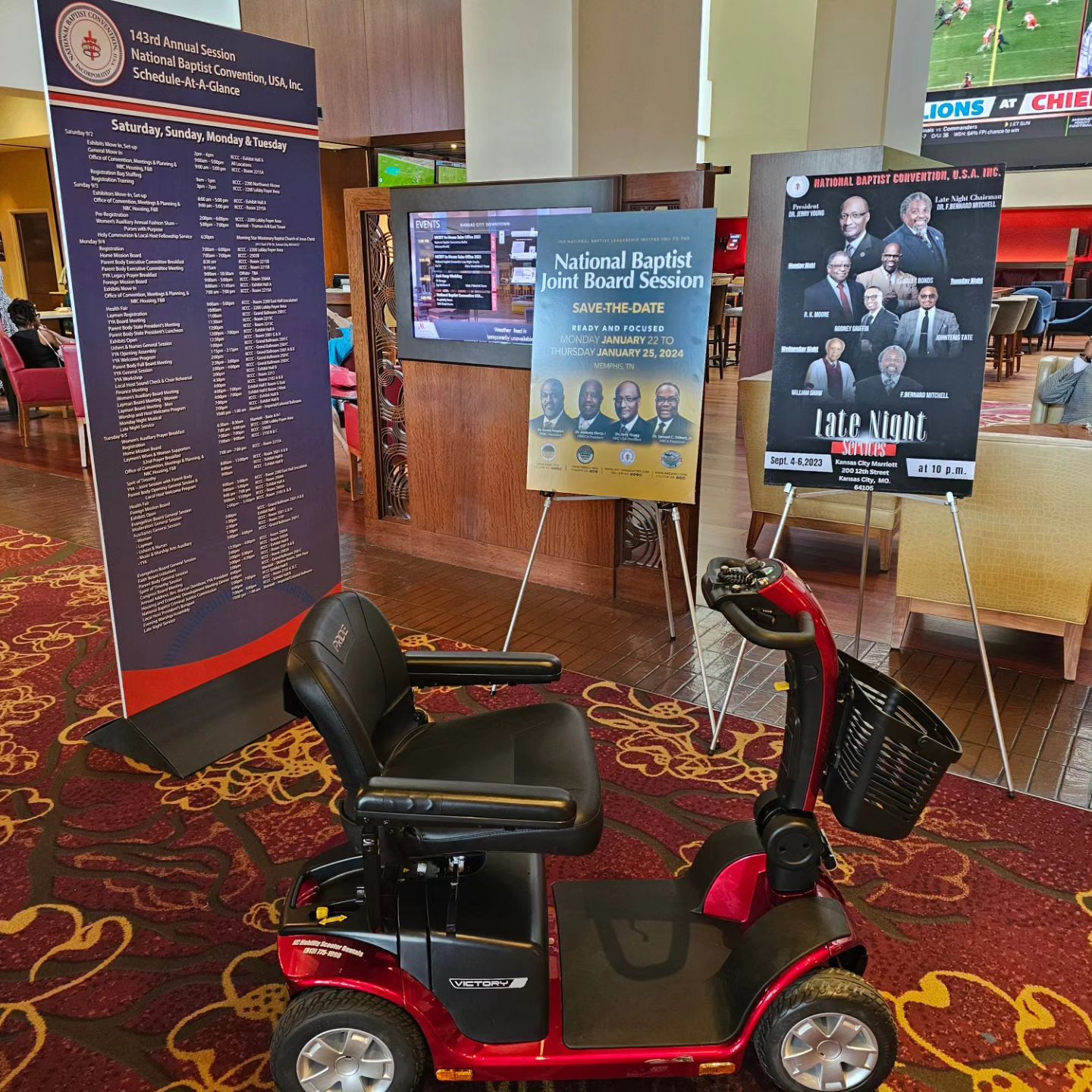 Indoor event space with informational posters, a mobility scooter, and seating area, possibly for a church or conference gathering.