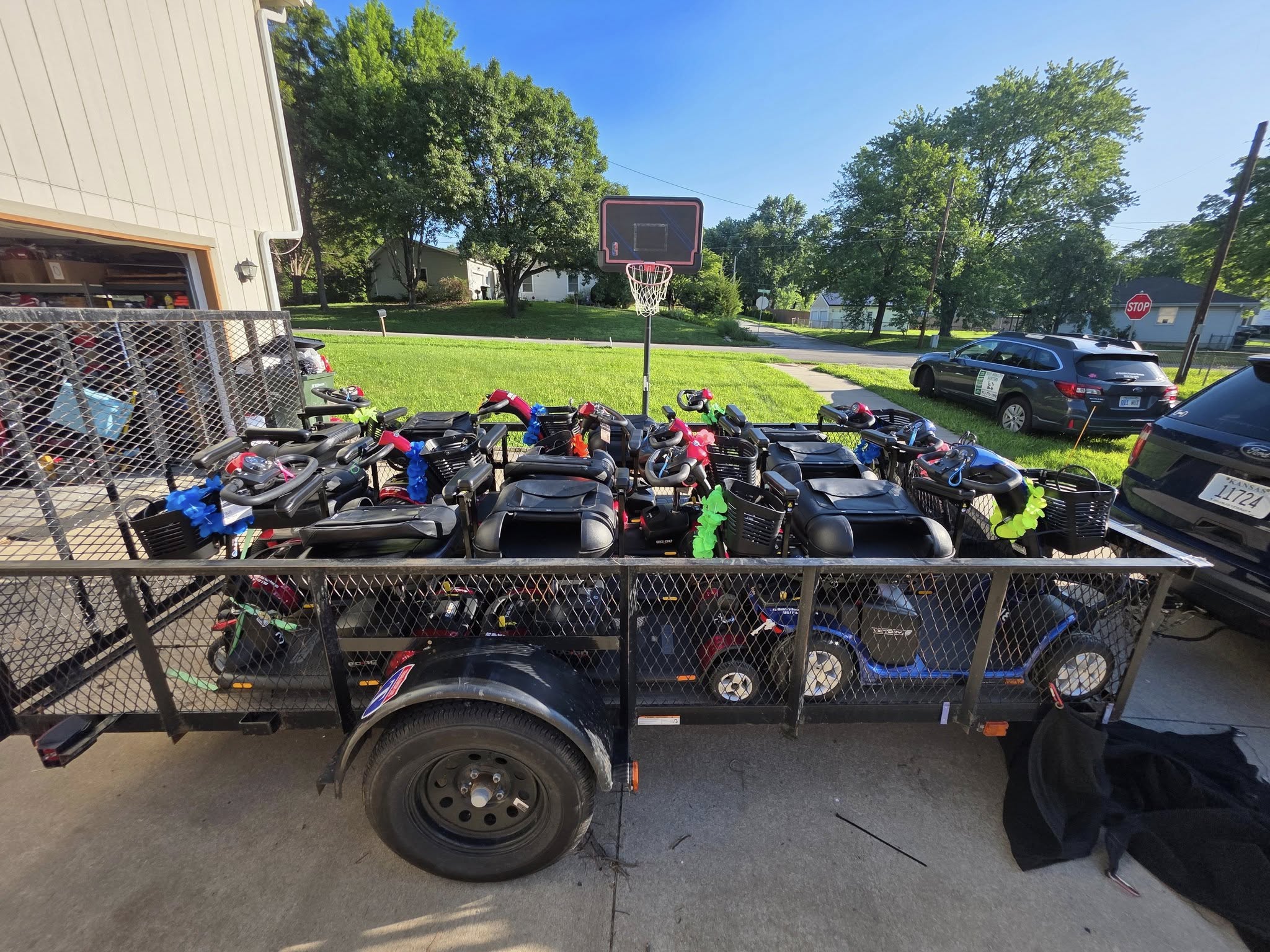 Multiple go-karts parked behind a fence outdoors, with trees, a basketball hoop, and cars in the background.