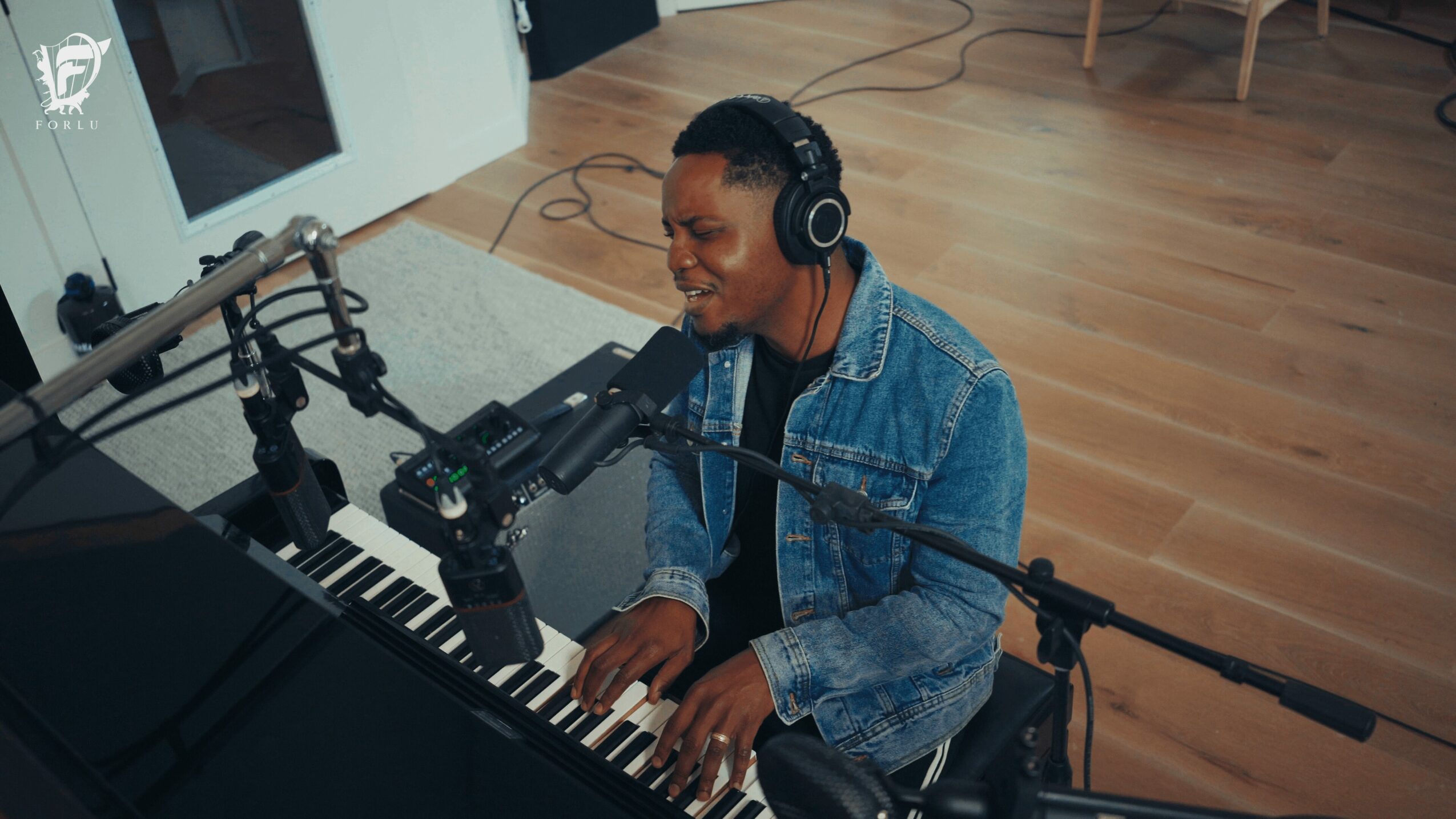Person playing piano, wearing headphones, smiling, in a recording studio with wooden floor and equipment.