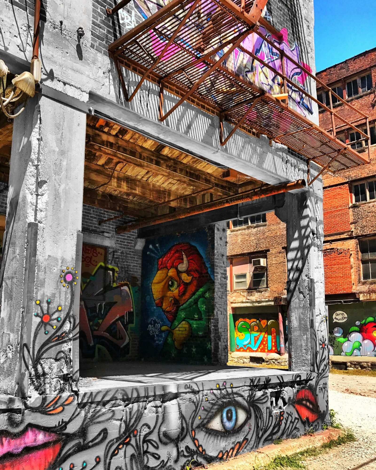 Street scene with graffiti art on a building wall, including a colorful face and eye, with a balcony above.