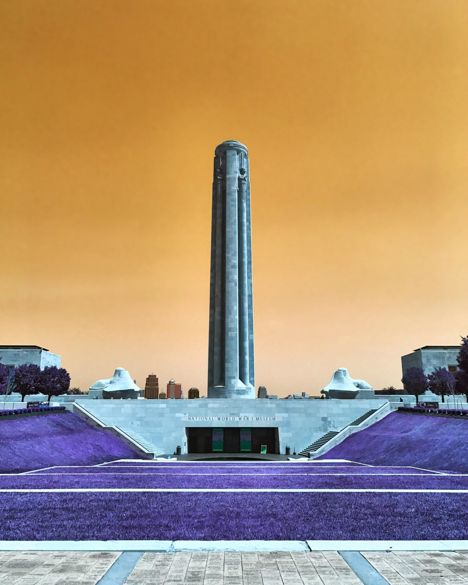 Tall monument with a wide base, set against an orange sky, with symmetrical structures and steps in front.