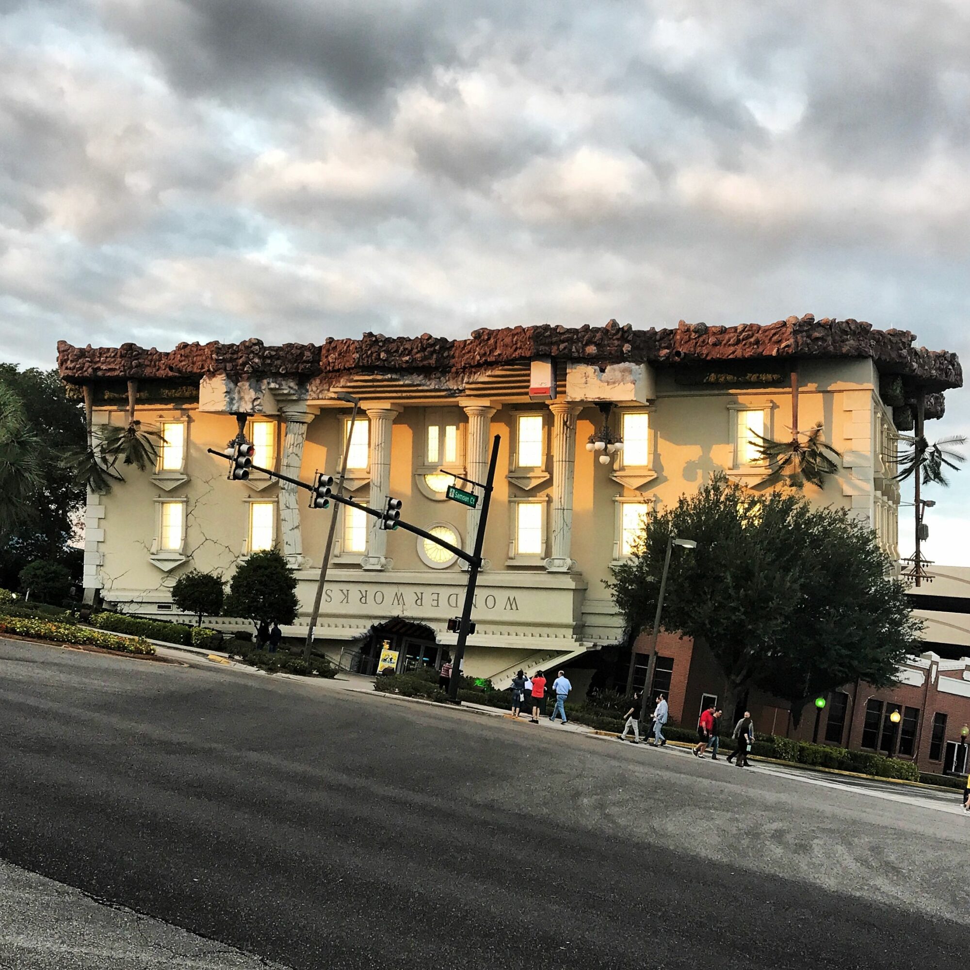 Street view of a building with a sign reading 'Woodworks,' trees, streetlights, and cloudy sky, upside down.