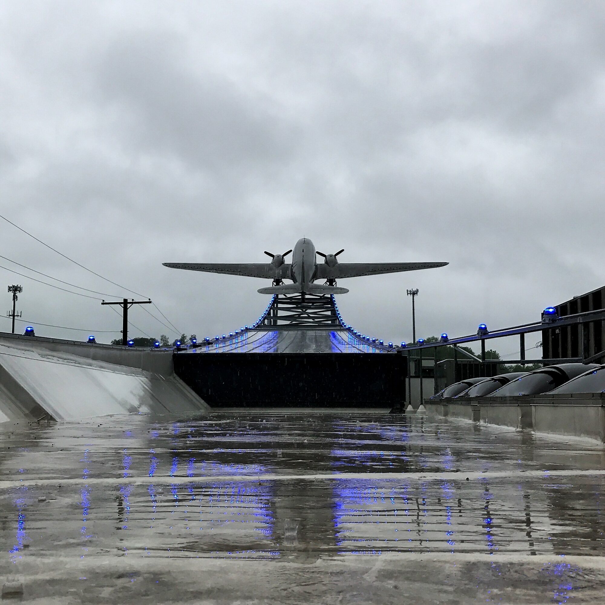 A monument of an airplane on a pedestal with water reflecting it, under a cloudy sky.