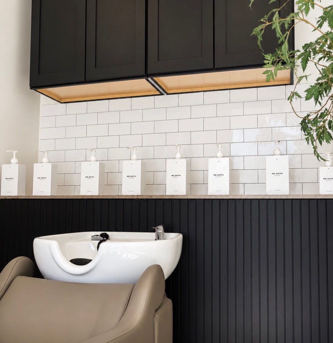 Bathroom with black cabinets, white subway tile wall, and a white sink with a beige chair in front.