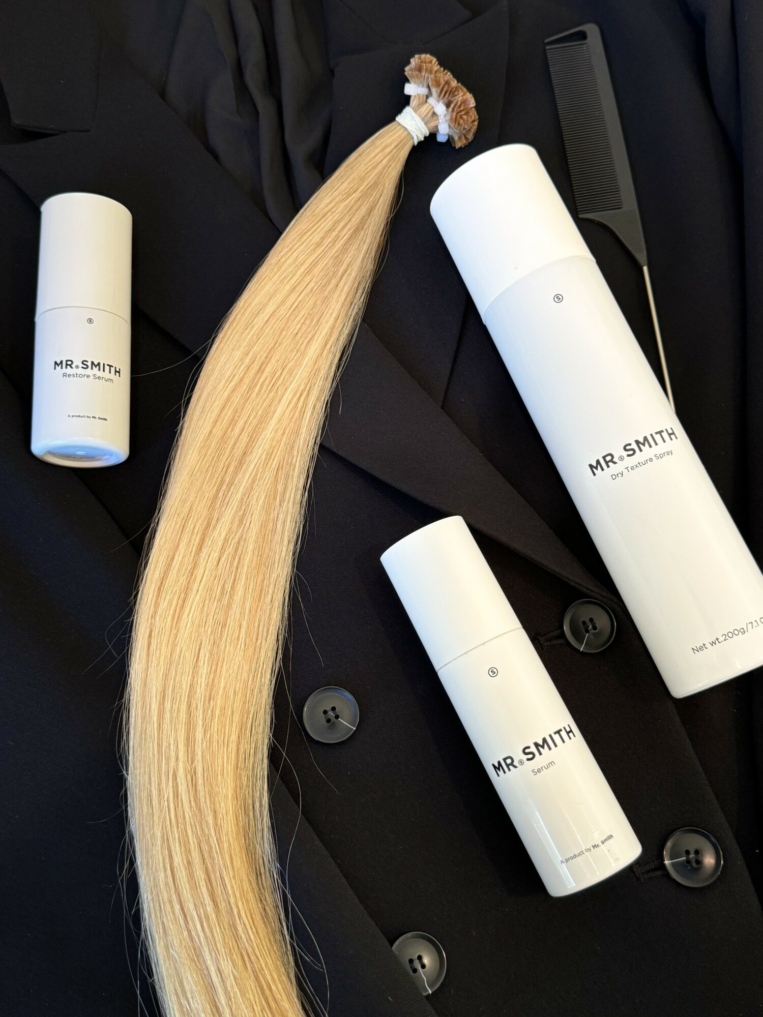 Blonde hair extension, hair spray, and a comb on a dark suit jacket.