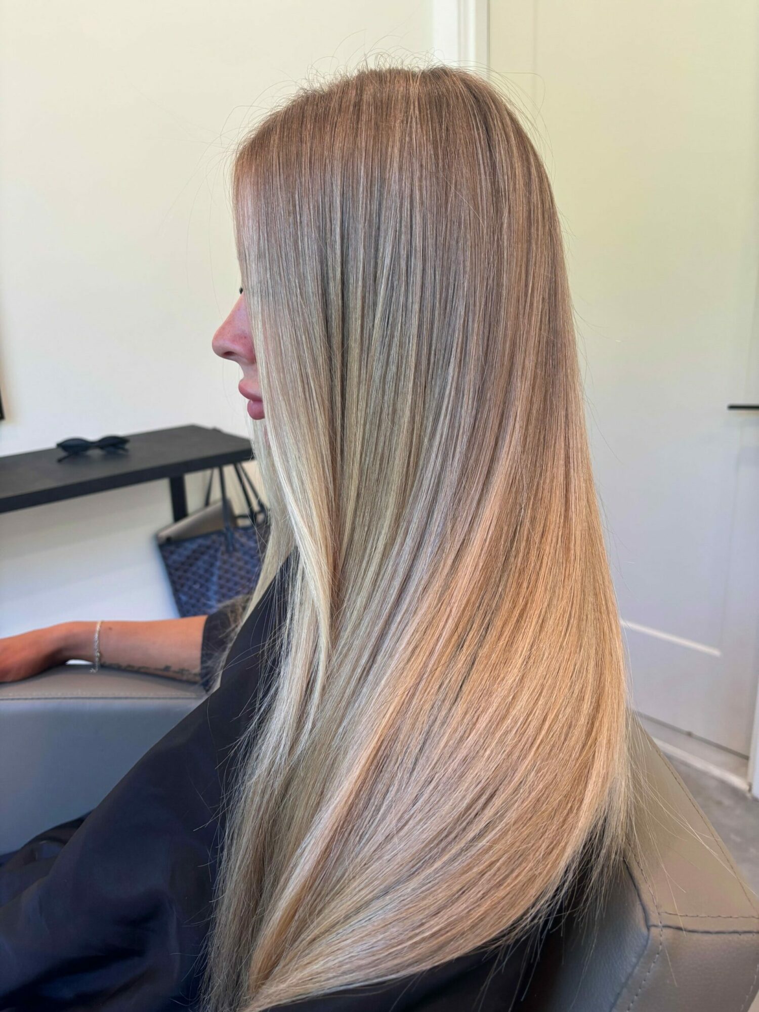 Side view of a person with long, straight, blonde hair sitting in a salon chair.