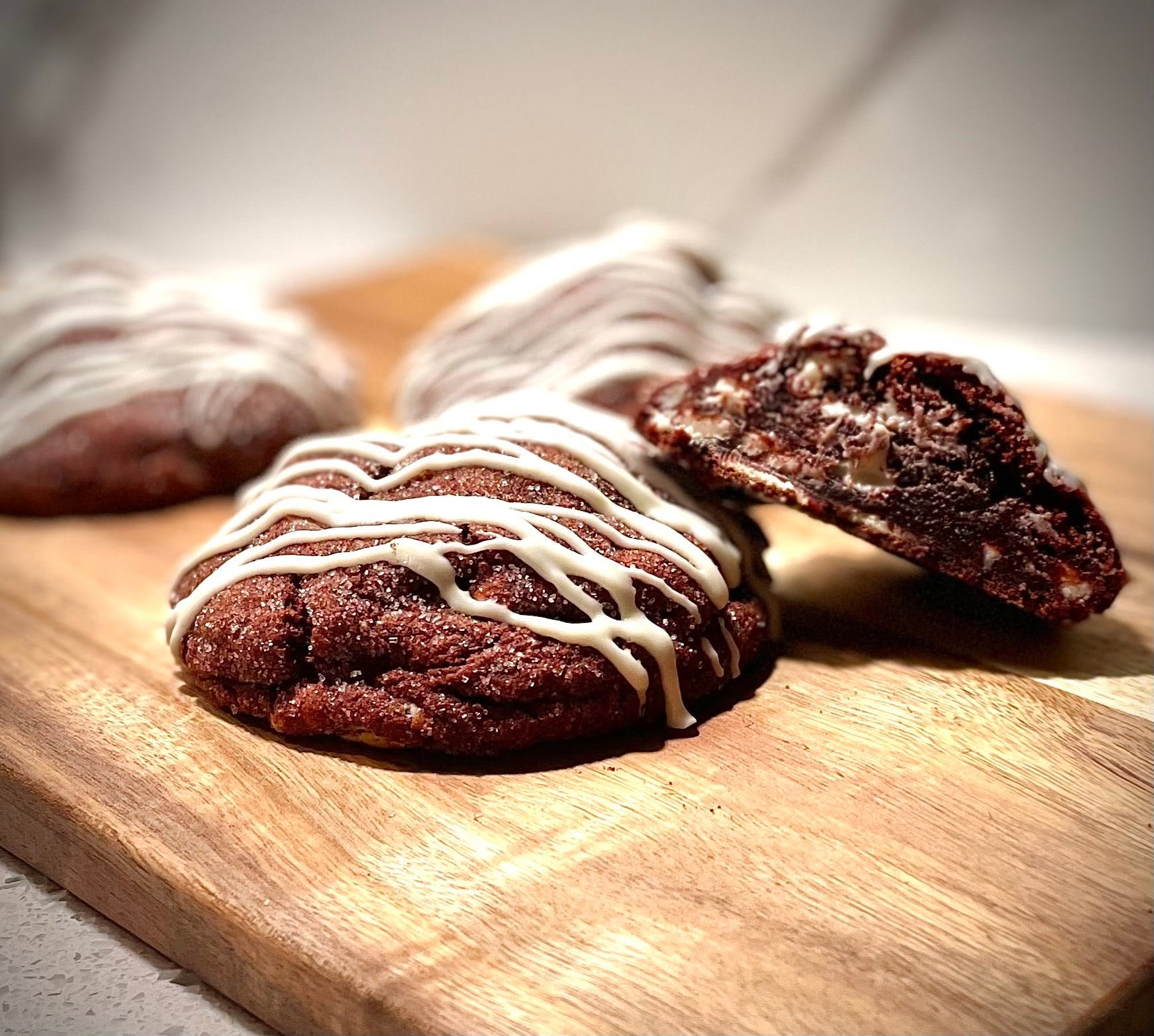 Chocolate cookies with white drizzle on a wooden surface, one broken to show inside, close-up view.