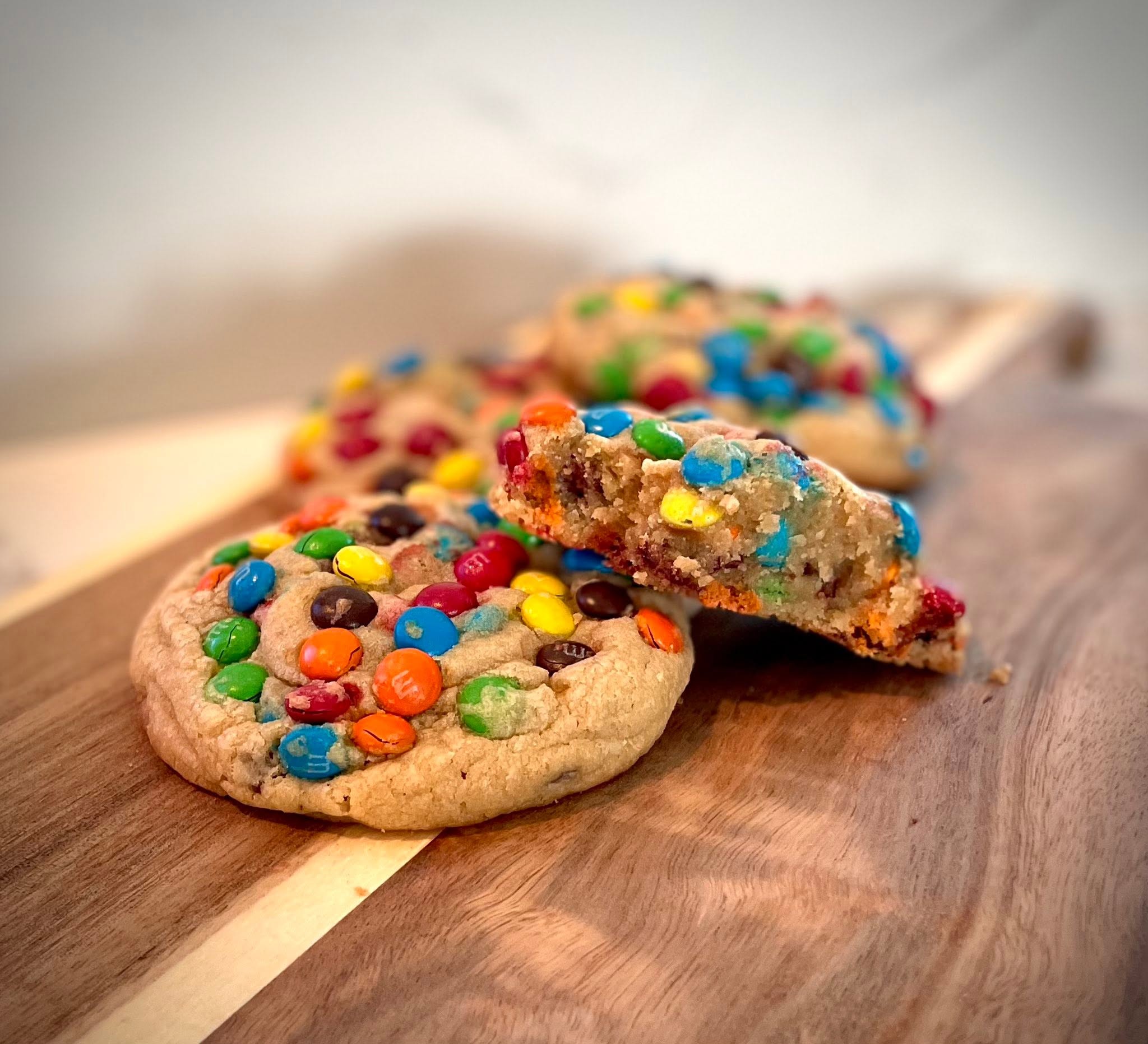 Two cookies with colorful candy toppings, one broken in half, on a wooden surface.