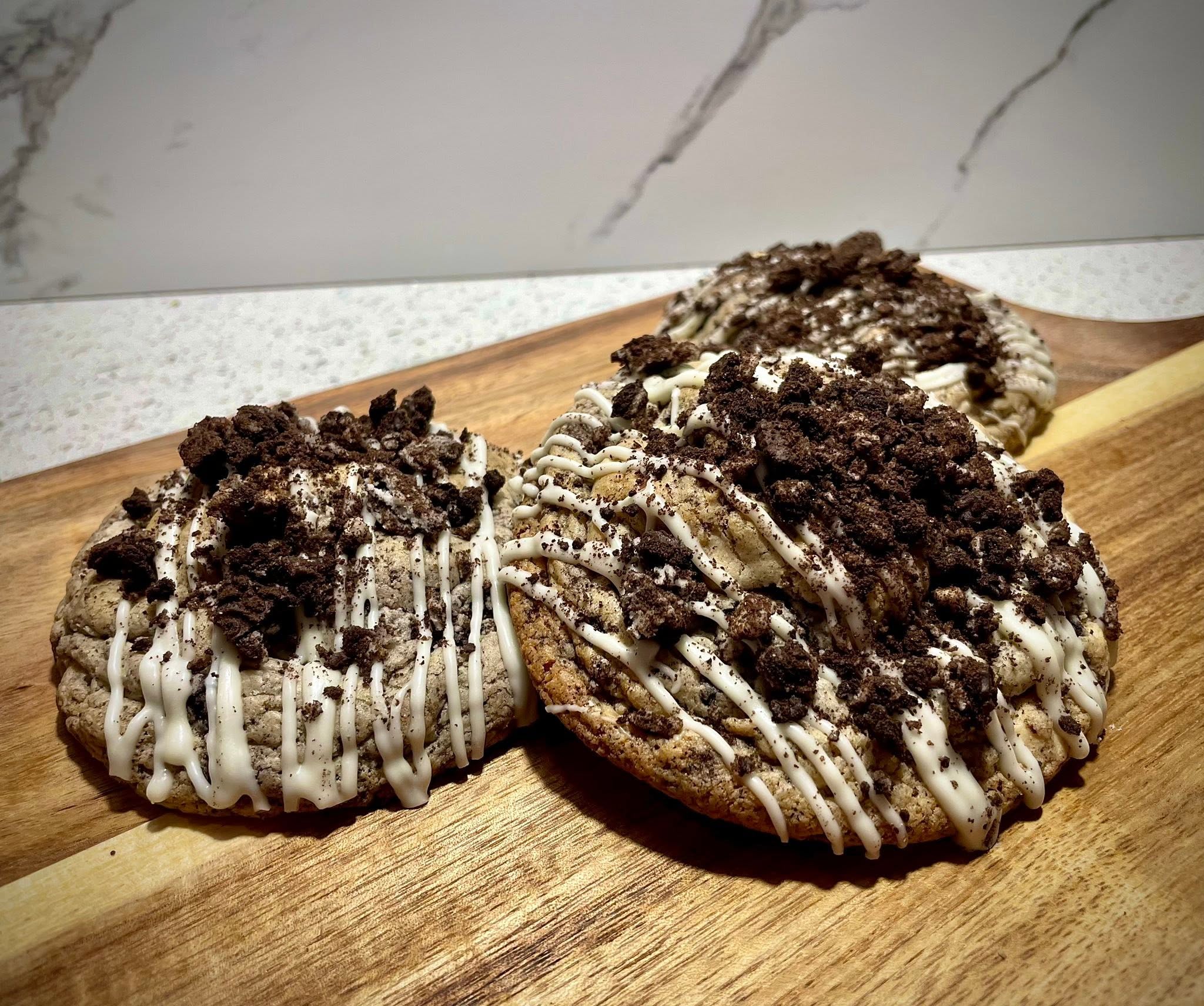 Three cookies with cream and chocolate crumbs on a wooden surface, with a marble wall background.
