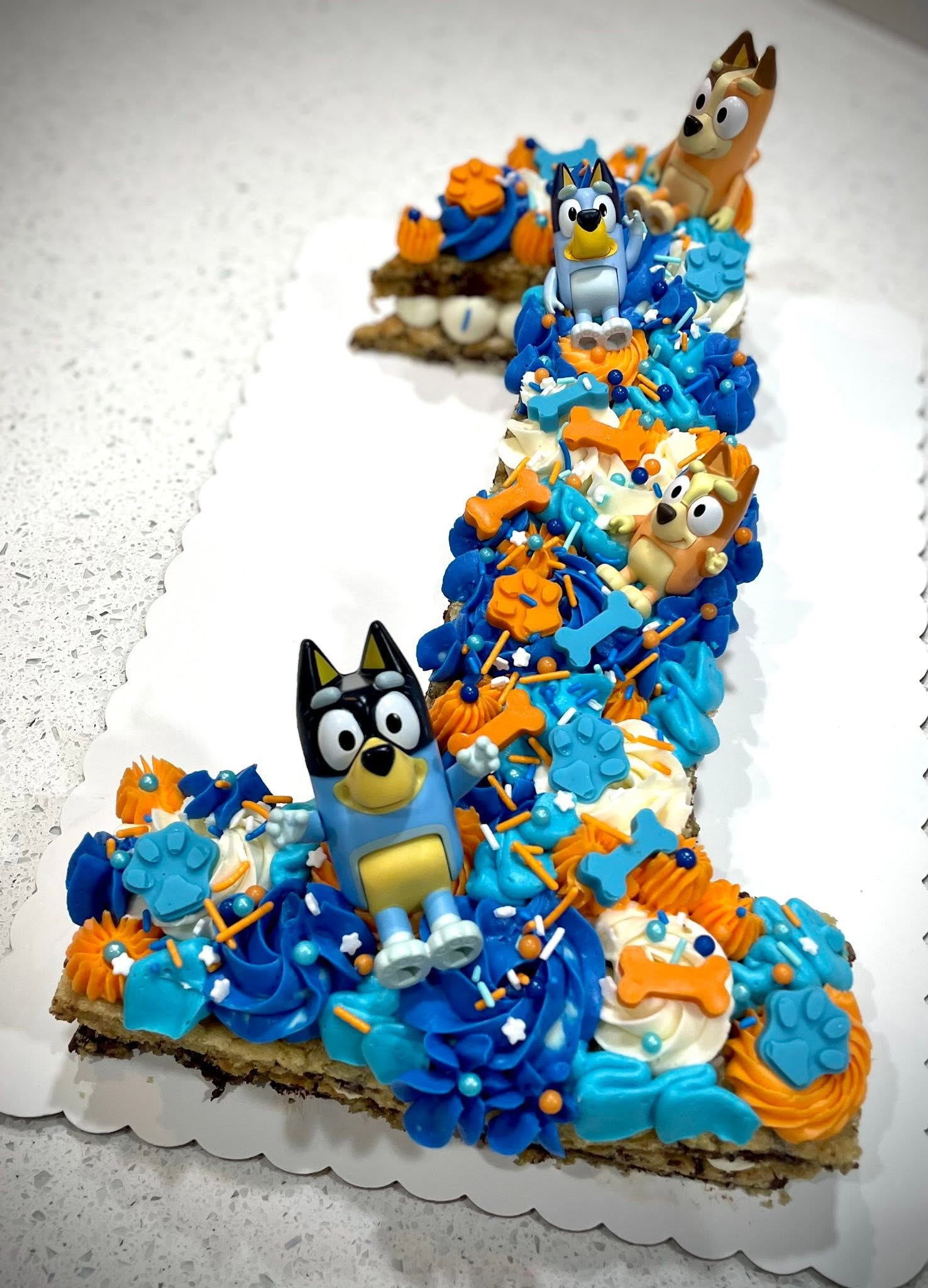 Number 1 cake decorated with blue, orange, and white icing, featuring cartoon animal toppers, on a white surface.