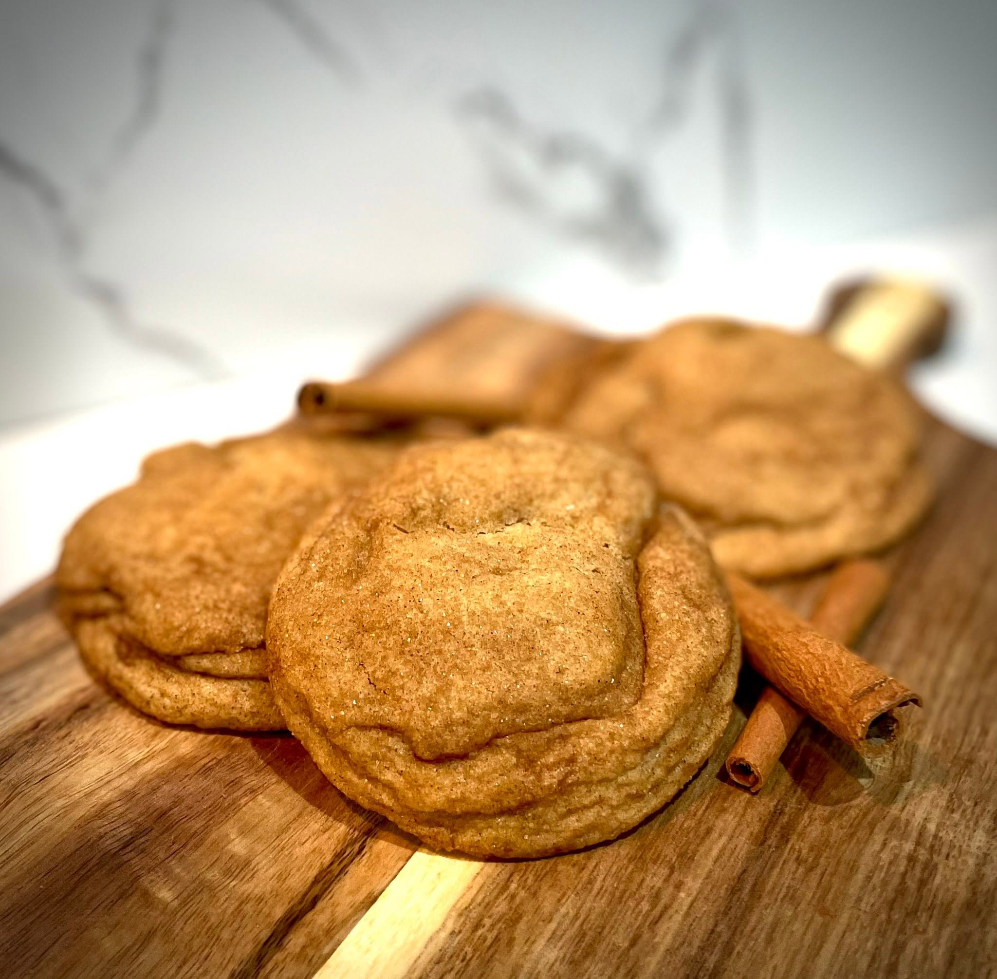 Three fried cookies on a wooden surface with cinnamon sticks, against a blurred white background.