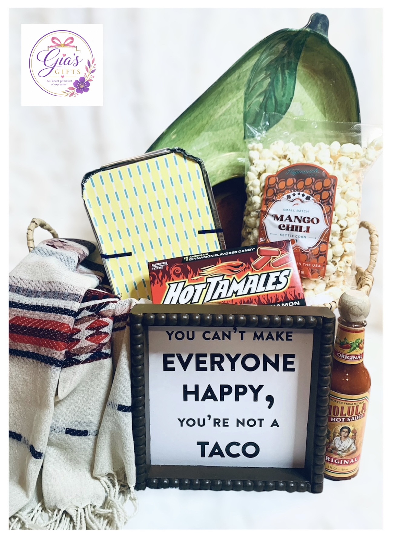 Basket with snacks, a framed sign, and a blanket, with a green bag and a jar of mango slices in the background.