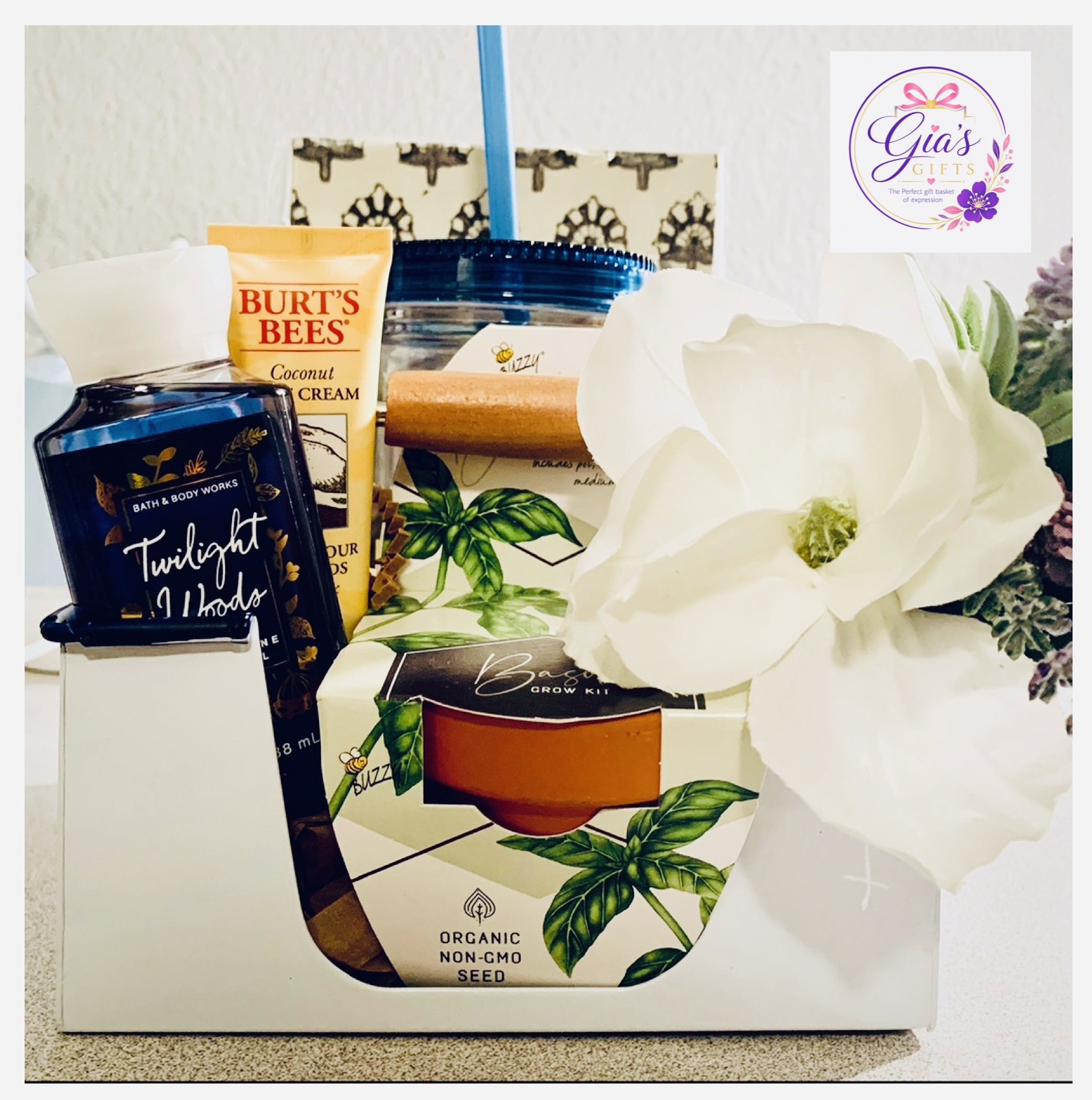 Gift box with Burt's Bees lotion, Twilight Woods body cream, a white flower, and decorative items, on a white surface.
