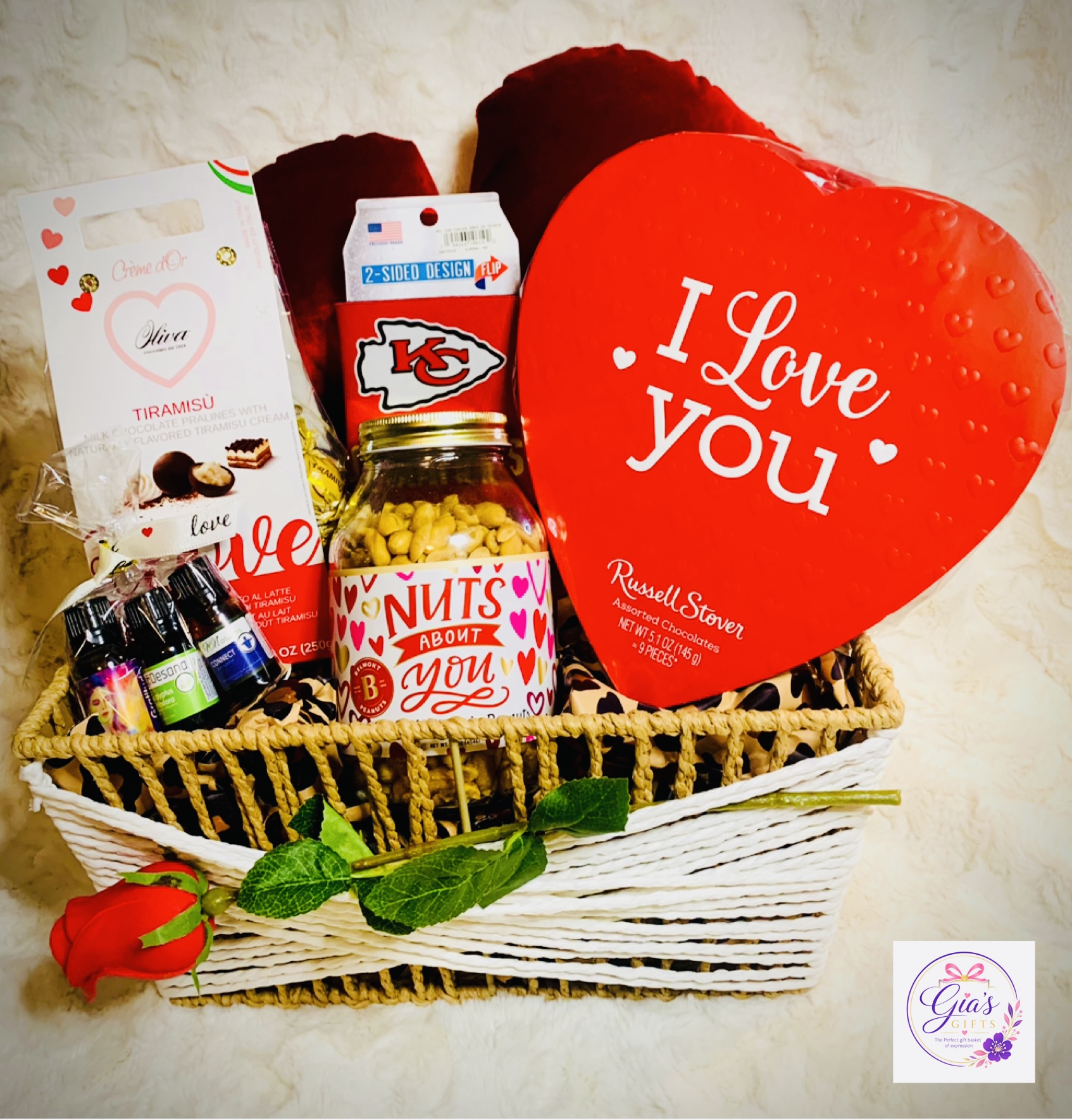Valentine's gift basket with a heart-shaped pillow, chocolates, and a small bouquet of roses and mint leaves, on a white background.