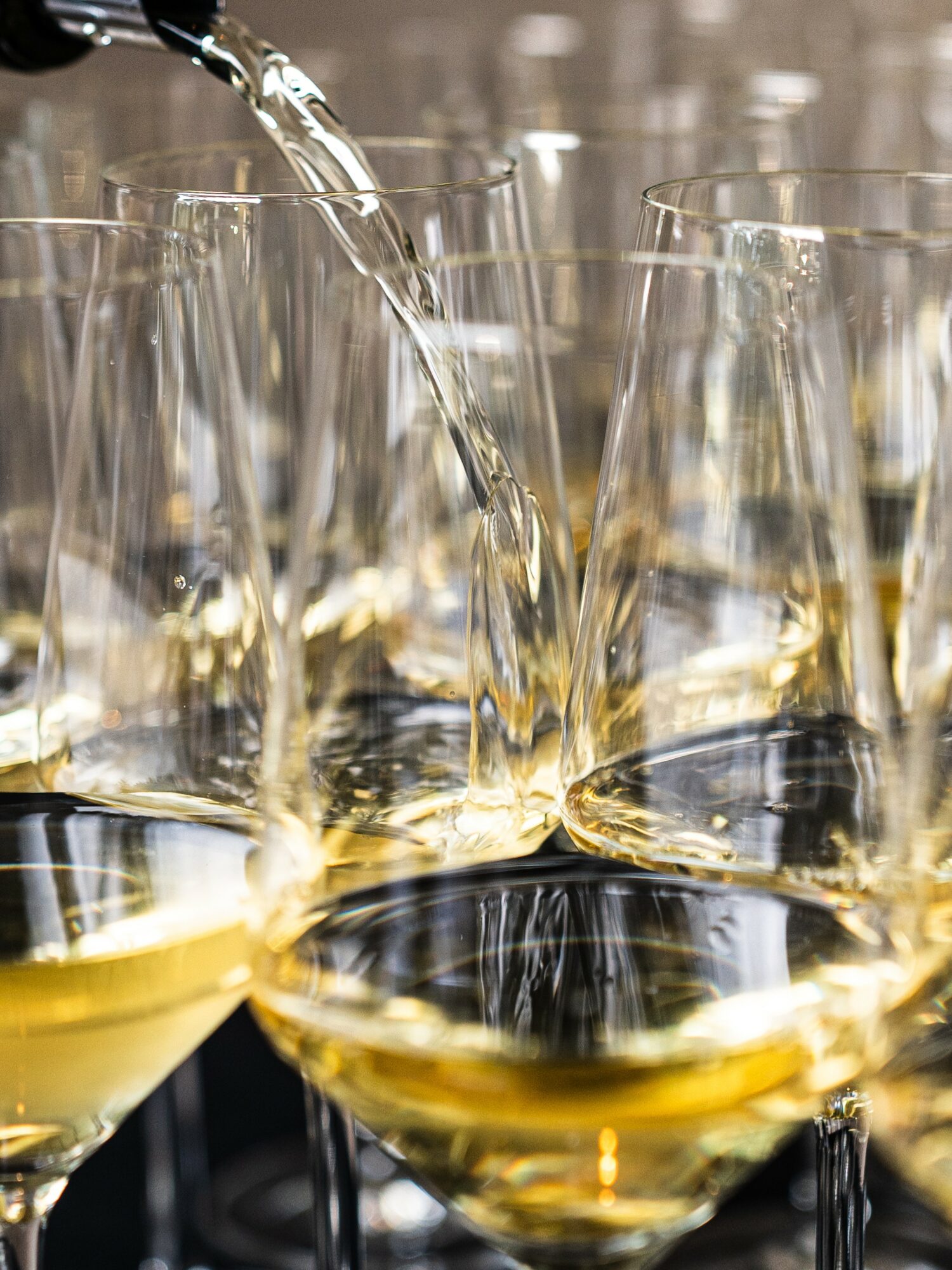 Pouring white wine into glasses, with several glasses filled and some empty, close-up view.