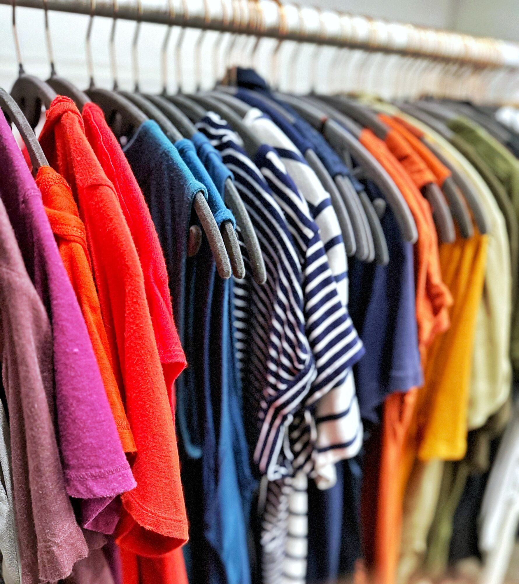 Clothes hanging on a rack, including striped, solid, and patterned shirts in various colors.