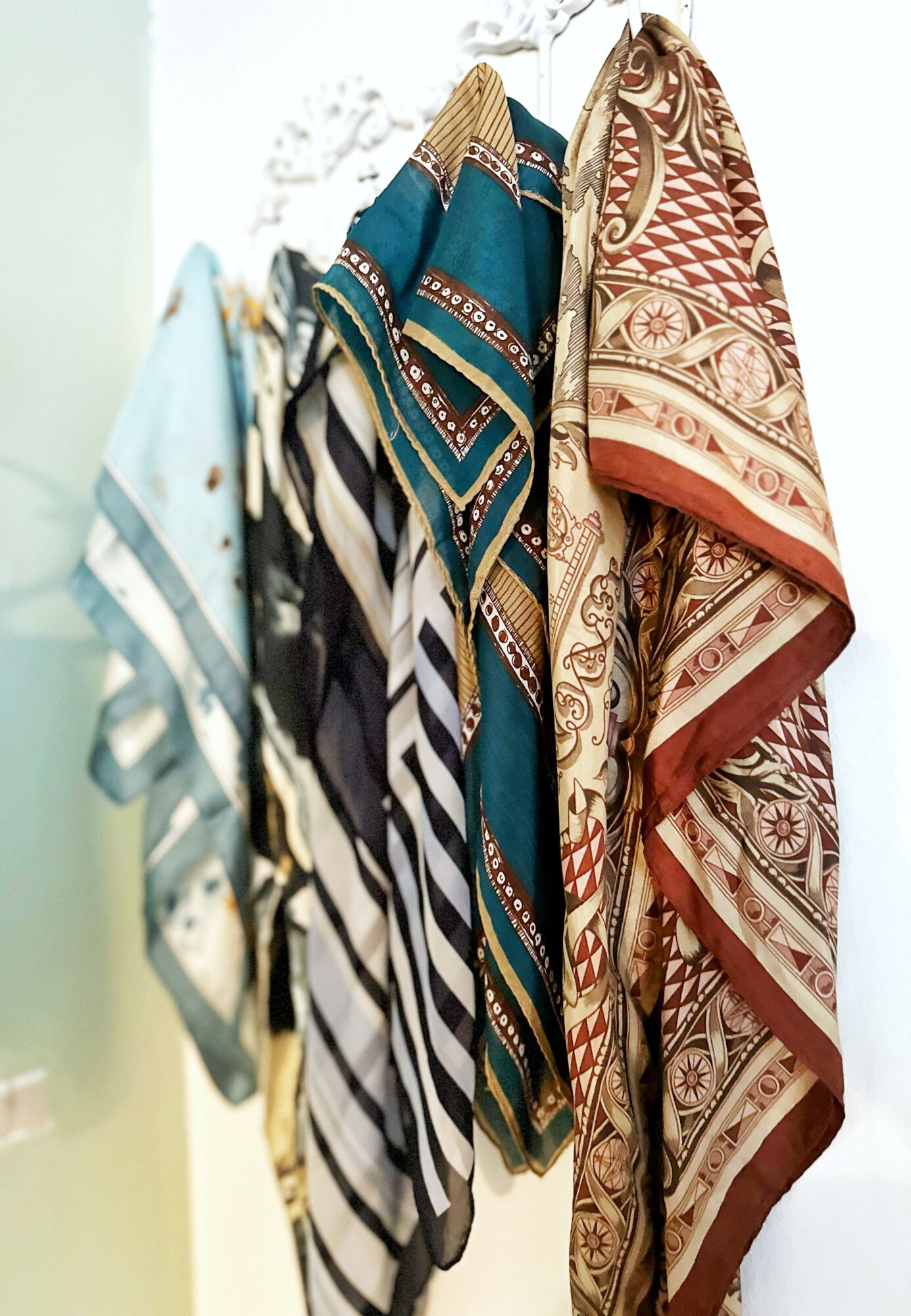 Two patterned scarves hanging side by side, one with blue and black stripes, the other with red and beige intricate designs.