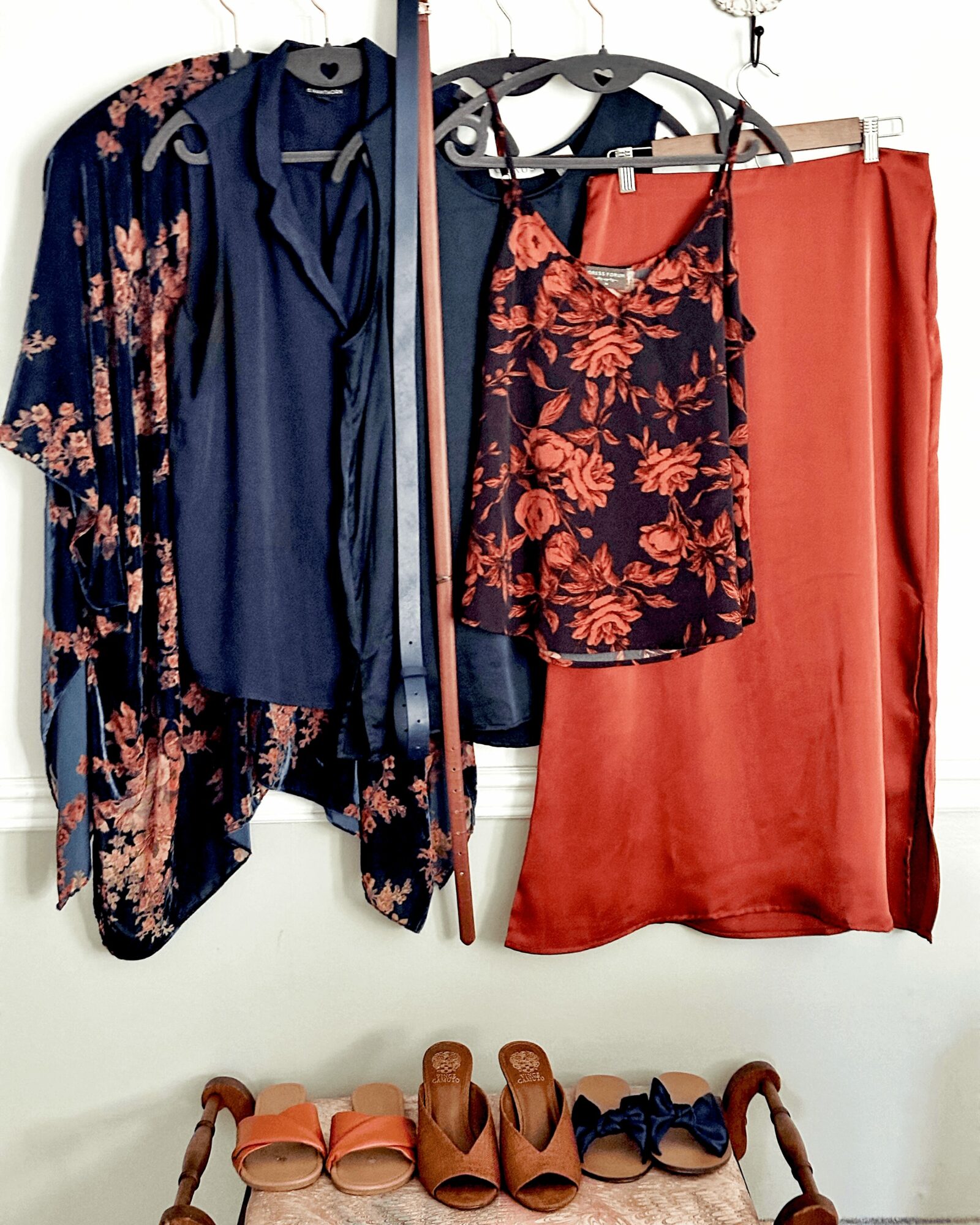Clothes hanging on a rack, including a floral kimono, a navy dress, a floral top, and a coral skirt, with shoes below.