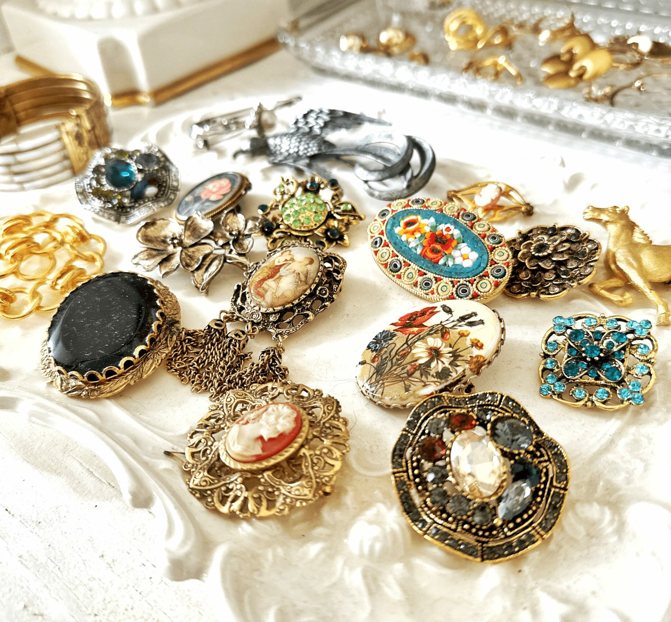 Collection of vintage and costume jewelry including brooches, rings, and pendants displayed on a white surface.