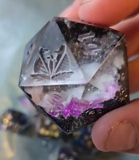 Hand holding a transparent, faceted cube with engraved symbols and purple inclusions inside.