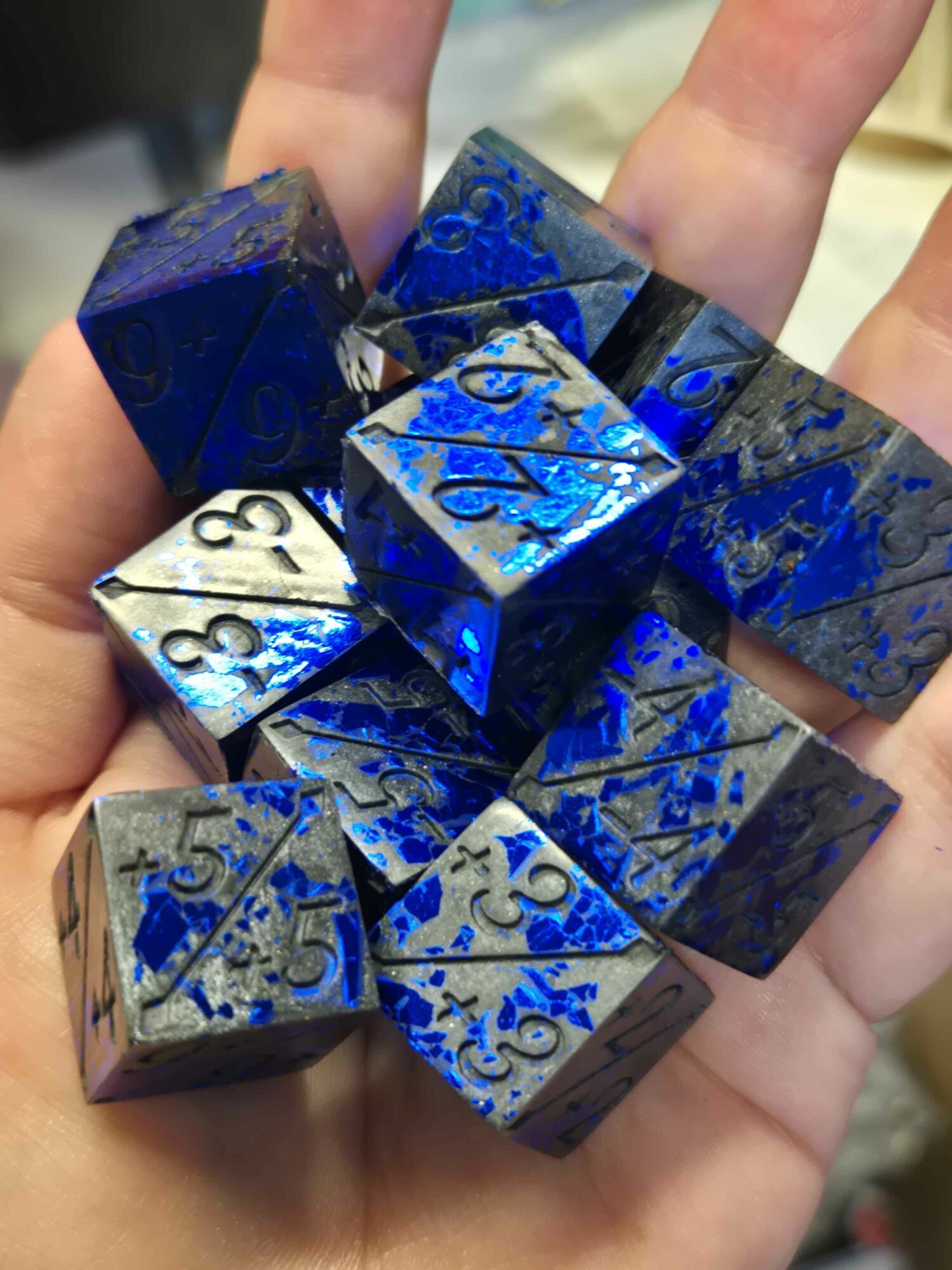 Hand holding shiny blue and black dice with intricate patterns, some showing numbers like 3, 4, and 8.